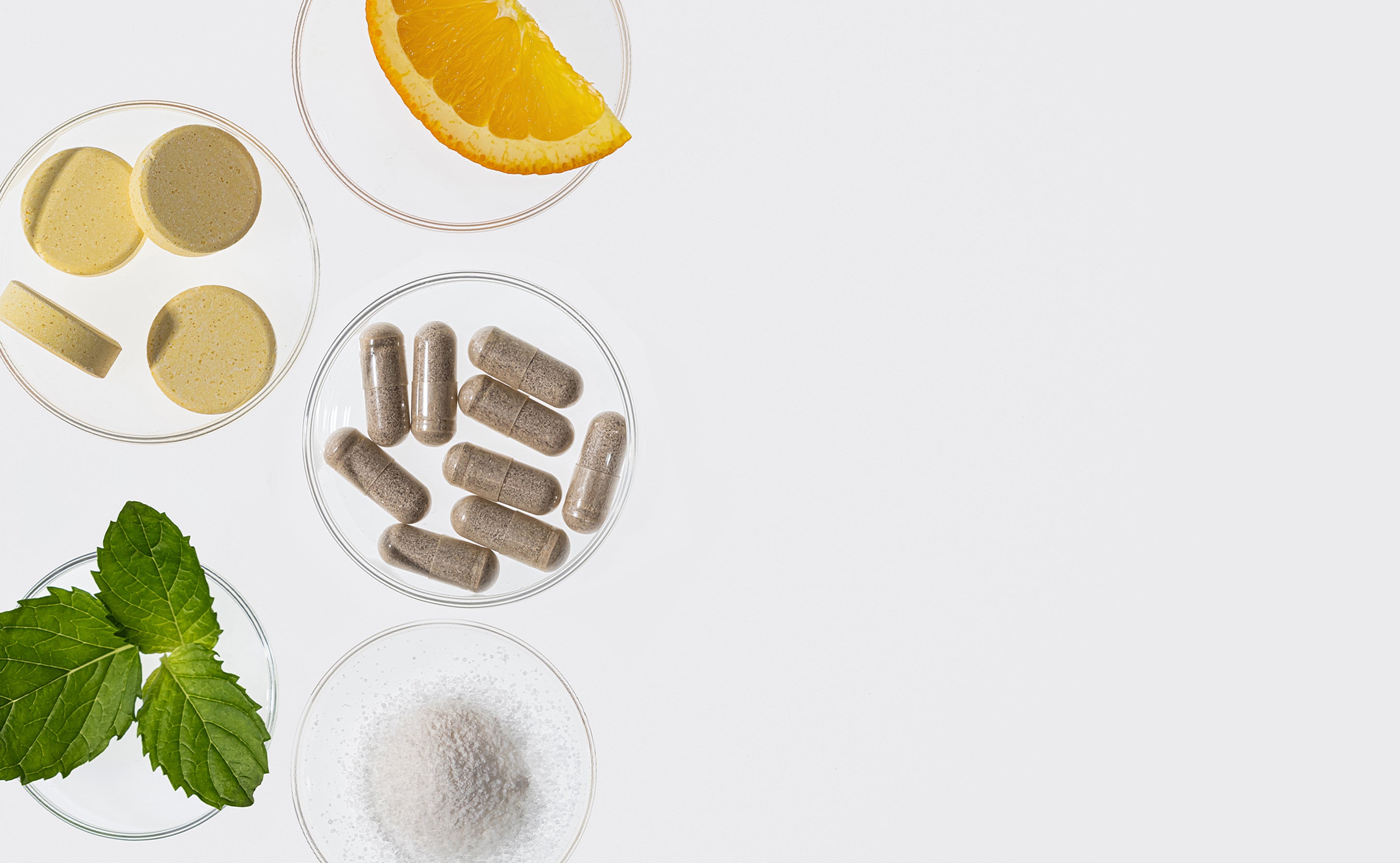 BrainMD Better Sleep Bundle: glass containers with capsules, tablets, powder, green leaves and orange slice on white surface