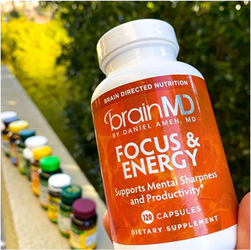 Supplement bottle labeled 'brainMD Focus & Energy' held in front of a row of other supplement bottles.