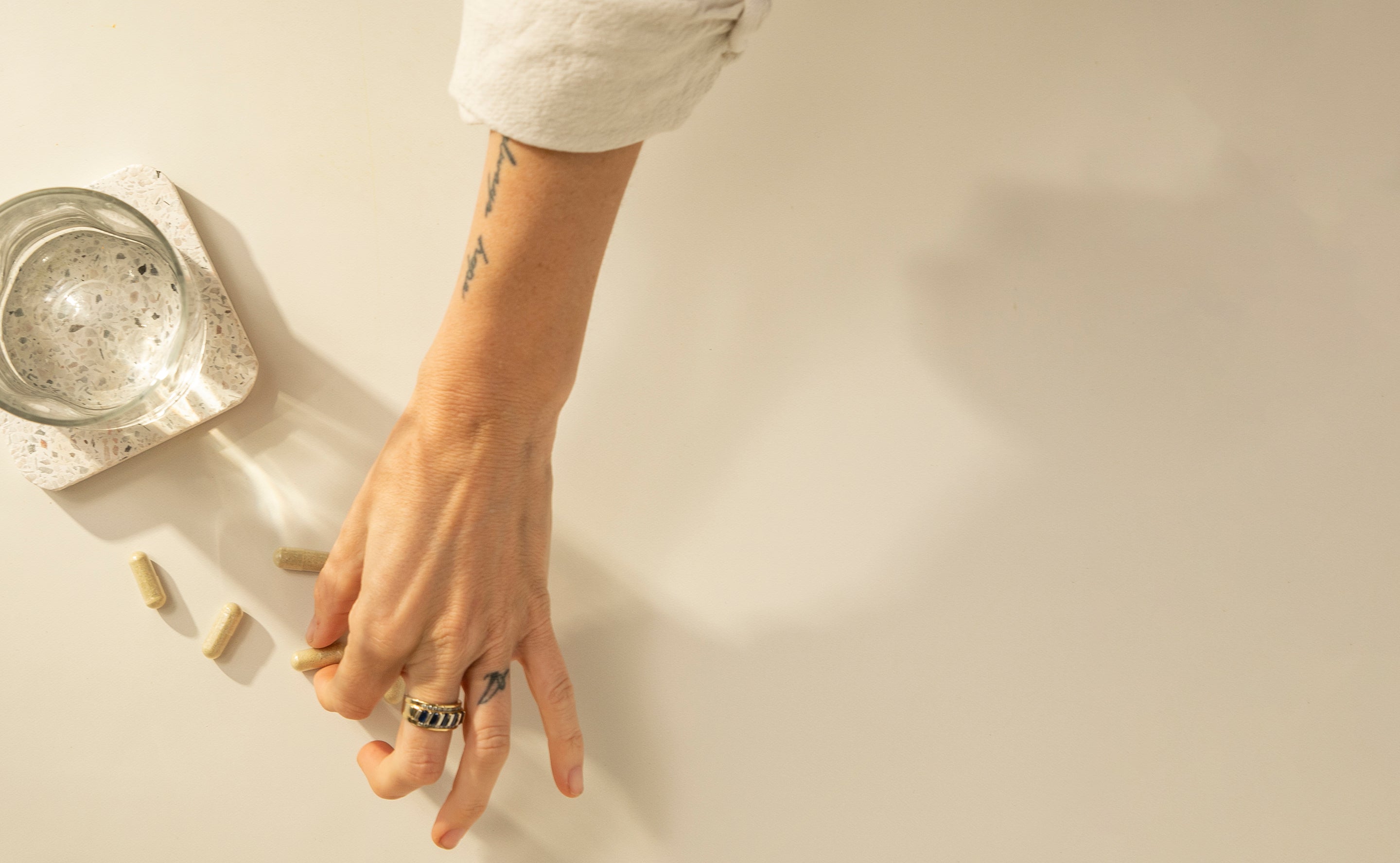 BrainMD Daily Essentials with Squeeze Bundle: person grabs a capsule next to a glass of water on cream-colored surface