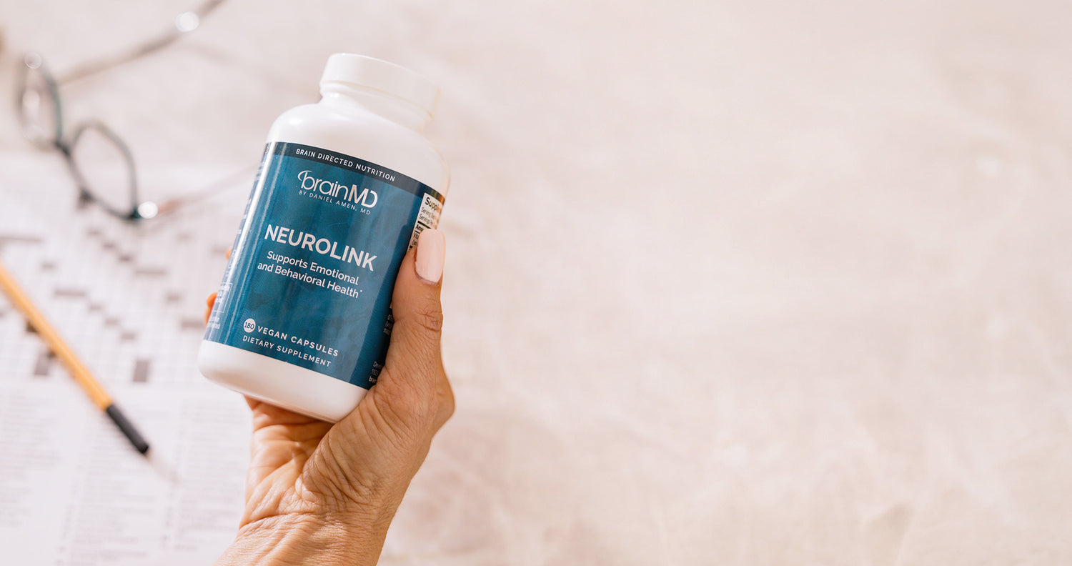 Hand holding a bottle of BrainMD NeuroLink supplement on a light background
