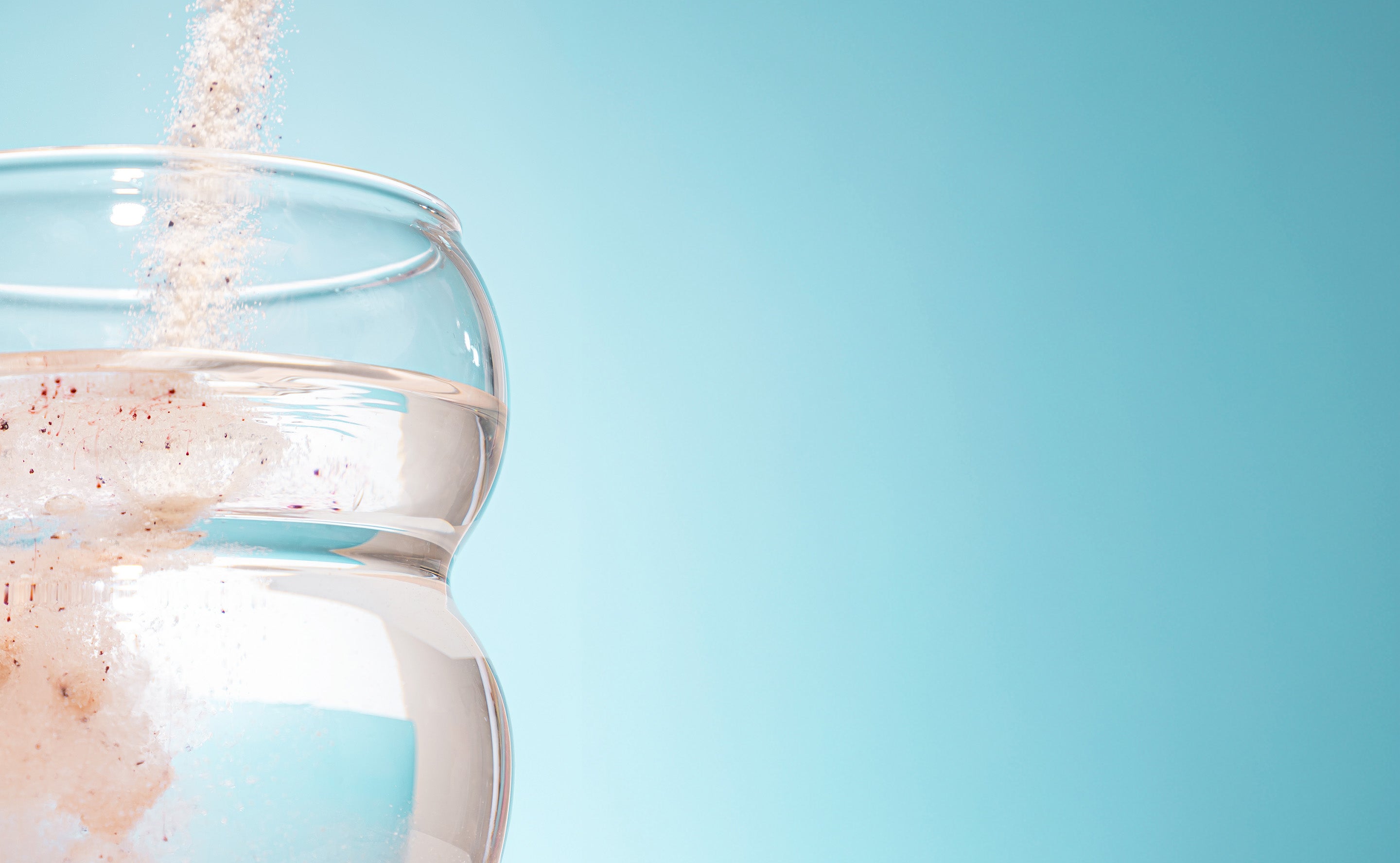 BrainMD Smart Electrolytes: powder being poured into a glass of water against a blue background