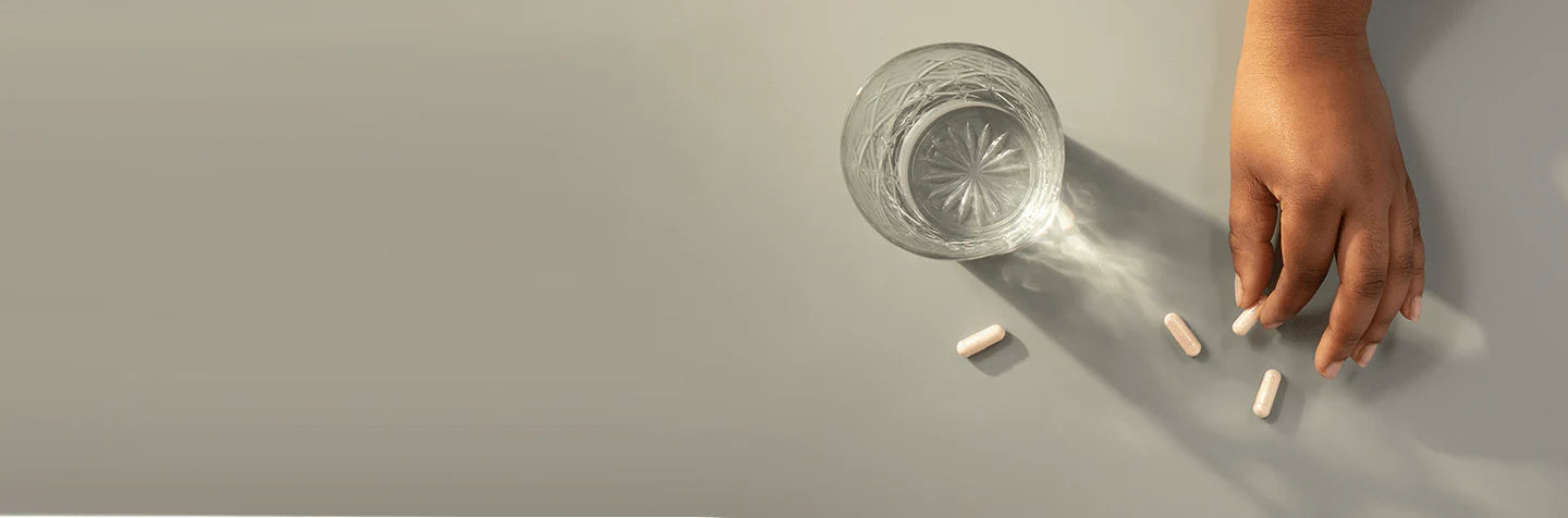 Hand holding a glass with scattered pills on a gray surface