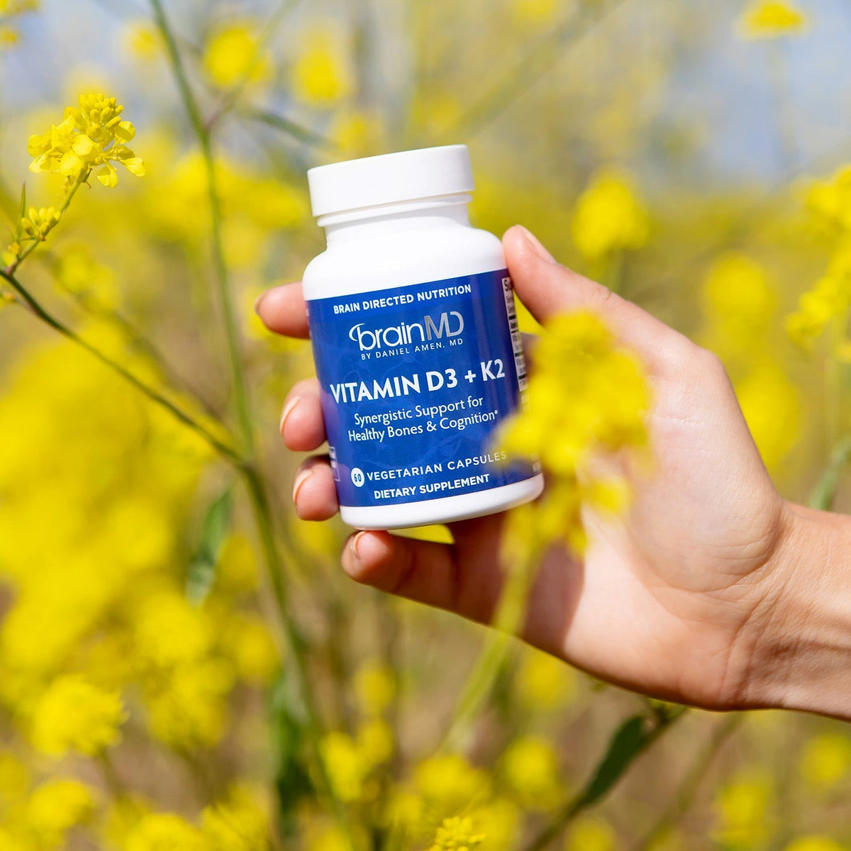Woman holding a BrainMD Vitamin D3 + K2 bottle against a sunny yellow background