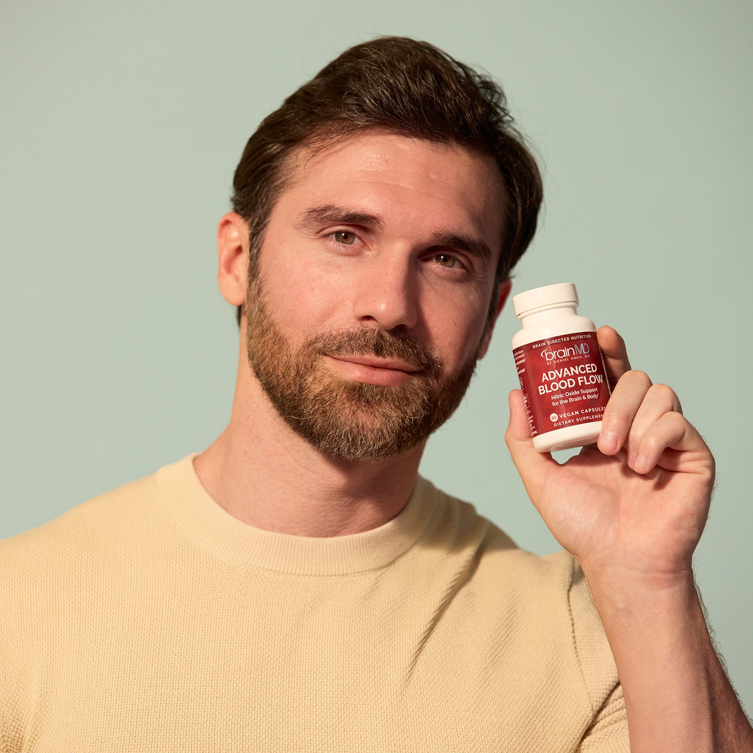 BrainMD 3-in-1 Brain Performance Bundle: man holding a red supplement bottle against a gray background