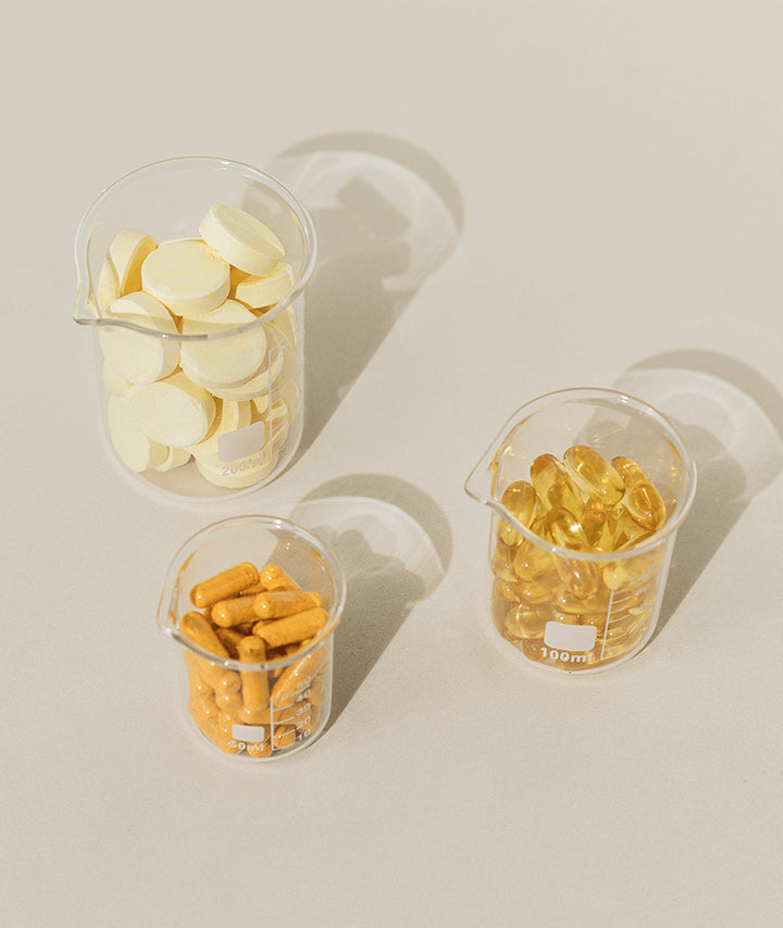 Three containers with tablets, softgels and capsules against an off-white background.