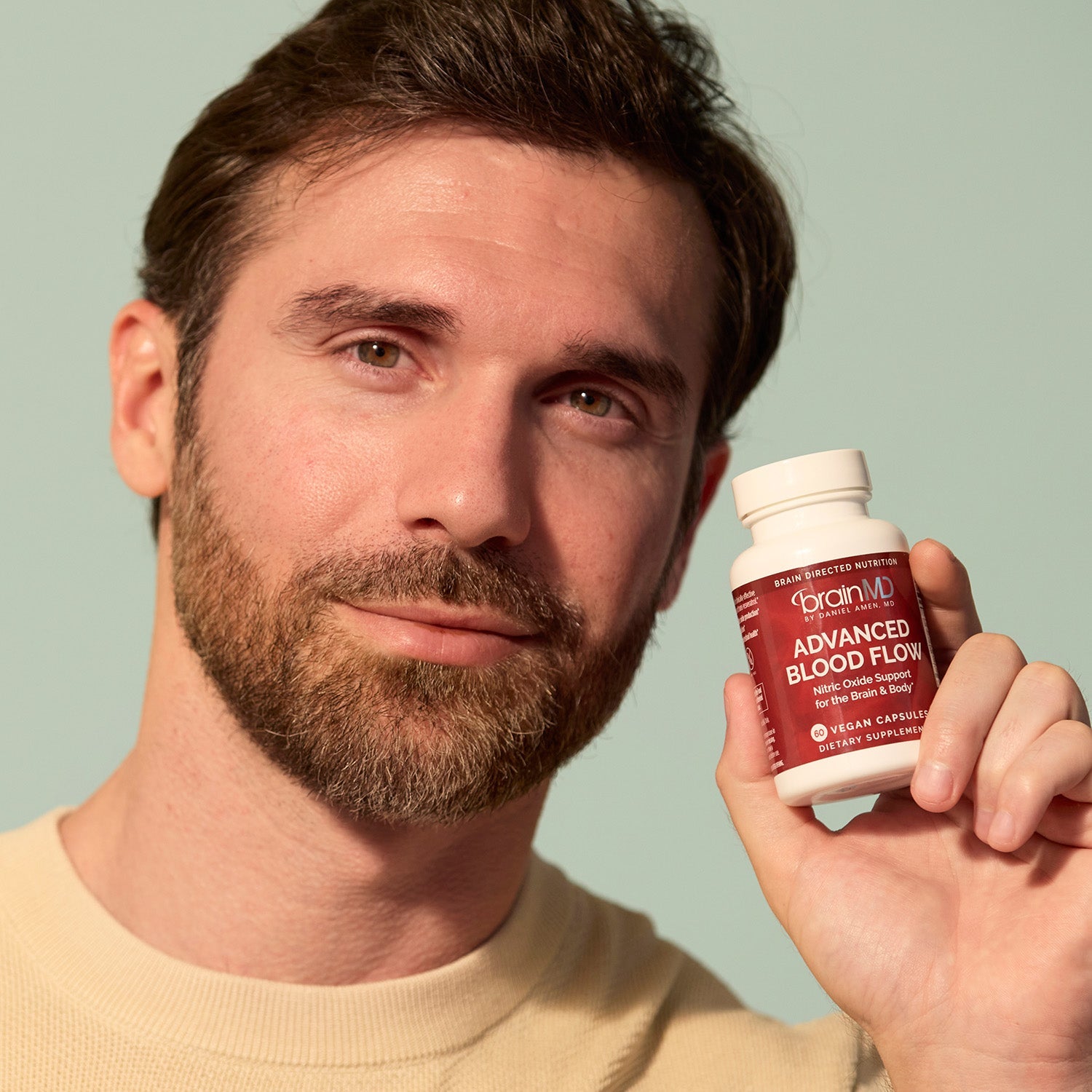 BrainMD Advanced Blood Flow: man holding supplement bottle with green background 