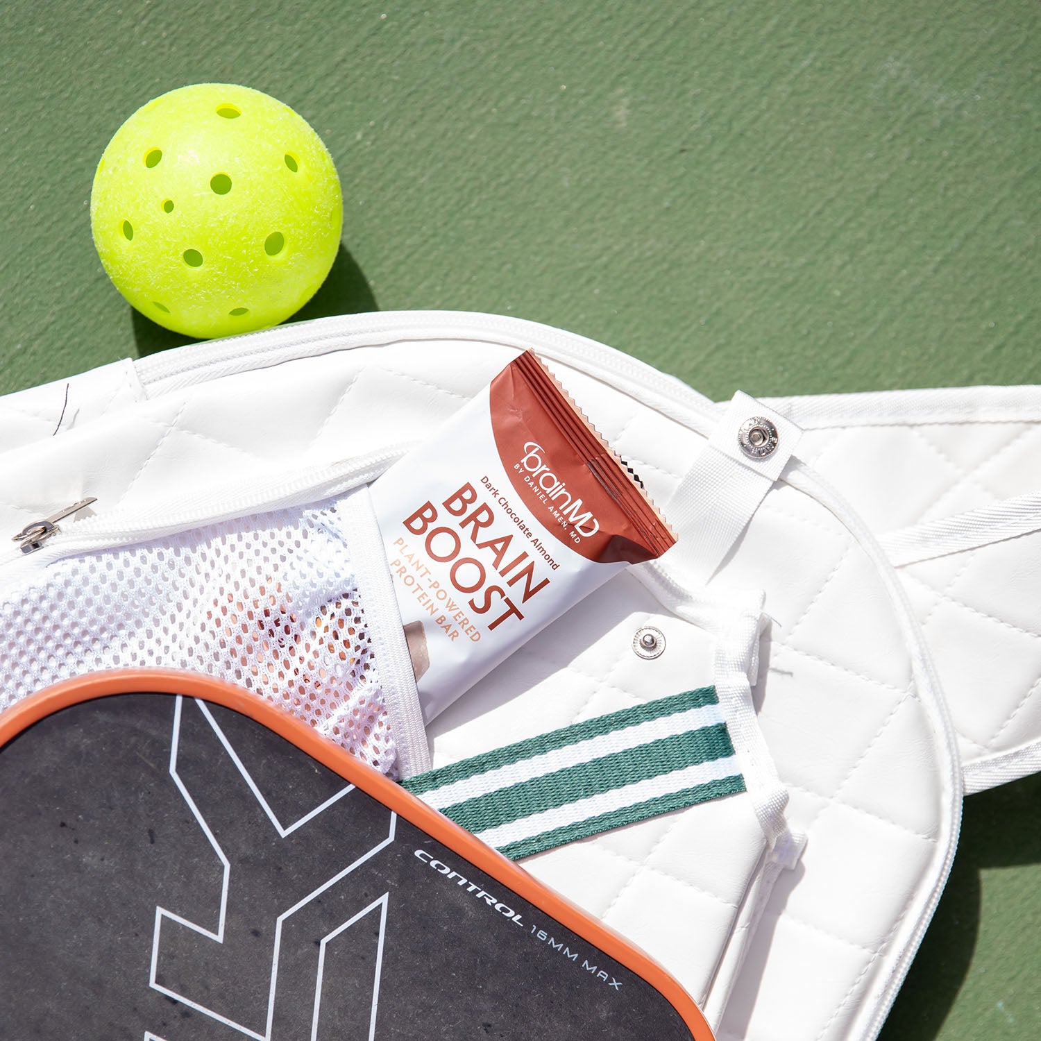 Pickleball racket and ball on a green court with a Brain Boost Protein Bar.