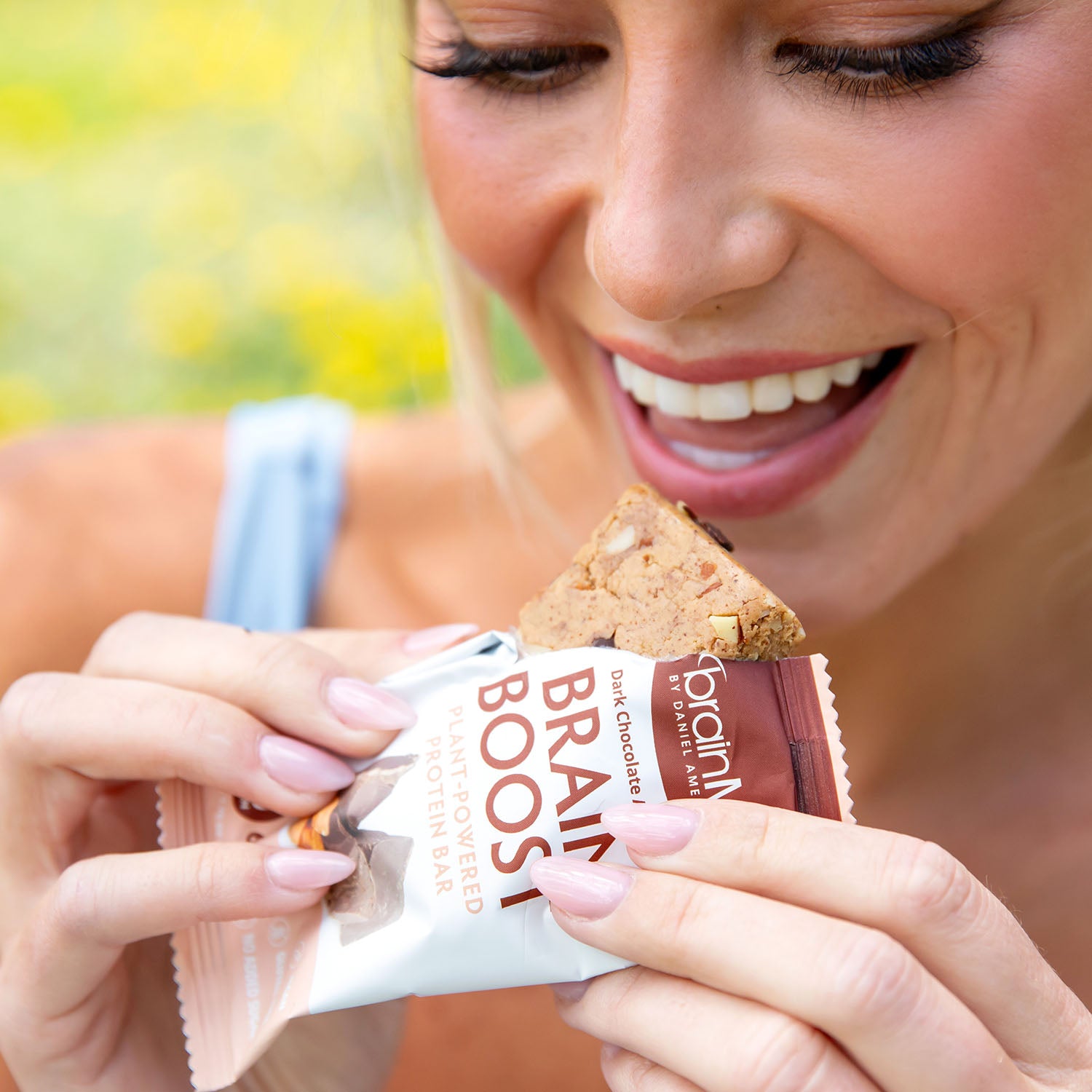 Woman preparing to take a bite of a Brain Boost Protein Bar.
