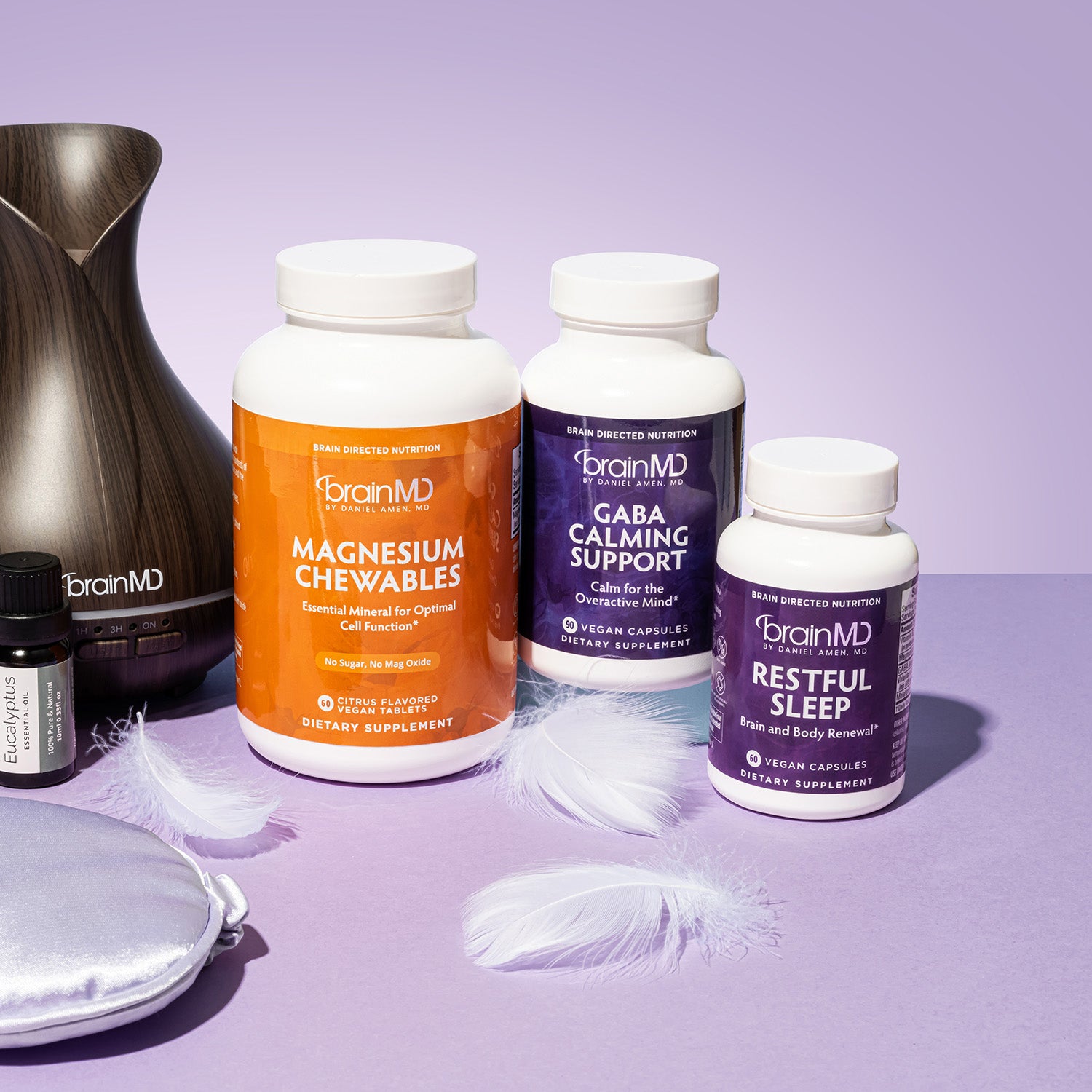 3 different supplement bottles with diffuser, essential oils and feathers against a lavender background.