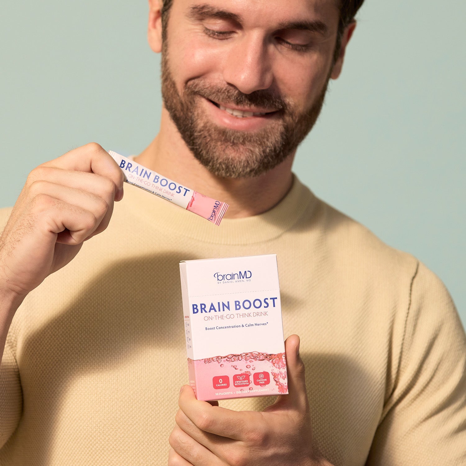 BrainMD Brain Boost On-The-Go: man holding a powder packet and a pink and white supplement box against a gray background