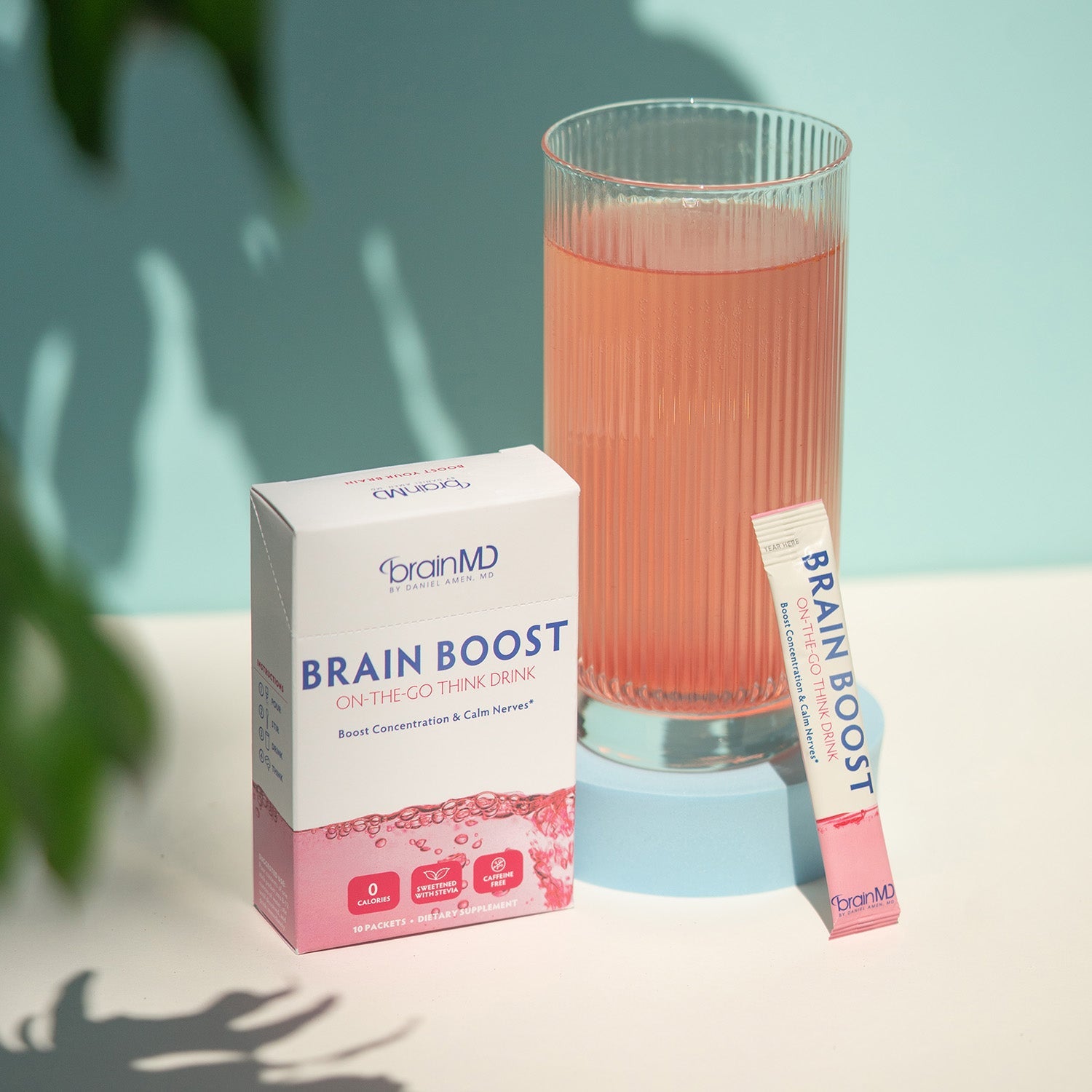 BrainMD Brain Boost On-The-Go: pink and white supplement box with powder packet leaning against a glass of pink water