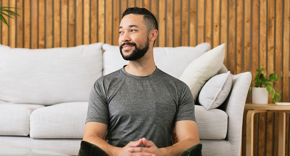 Man sitting on a couch in a living room with a wooden wall background