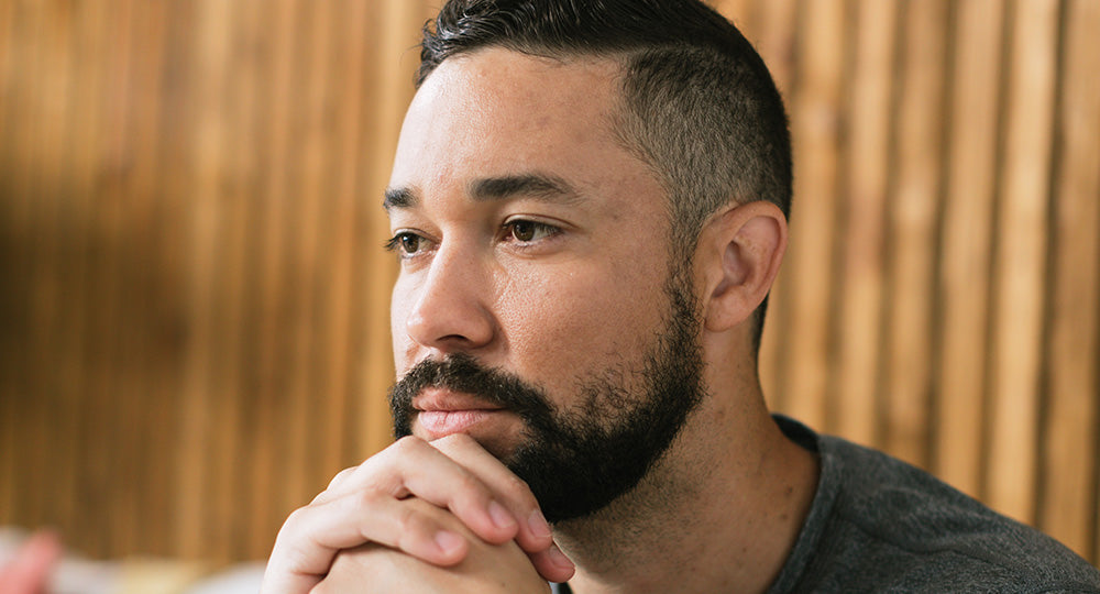 Man with a beard and short hair looking to the side with a wooden panel background