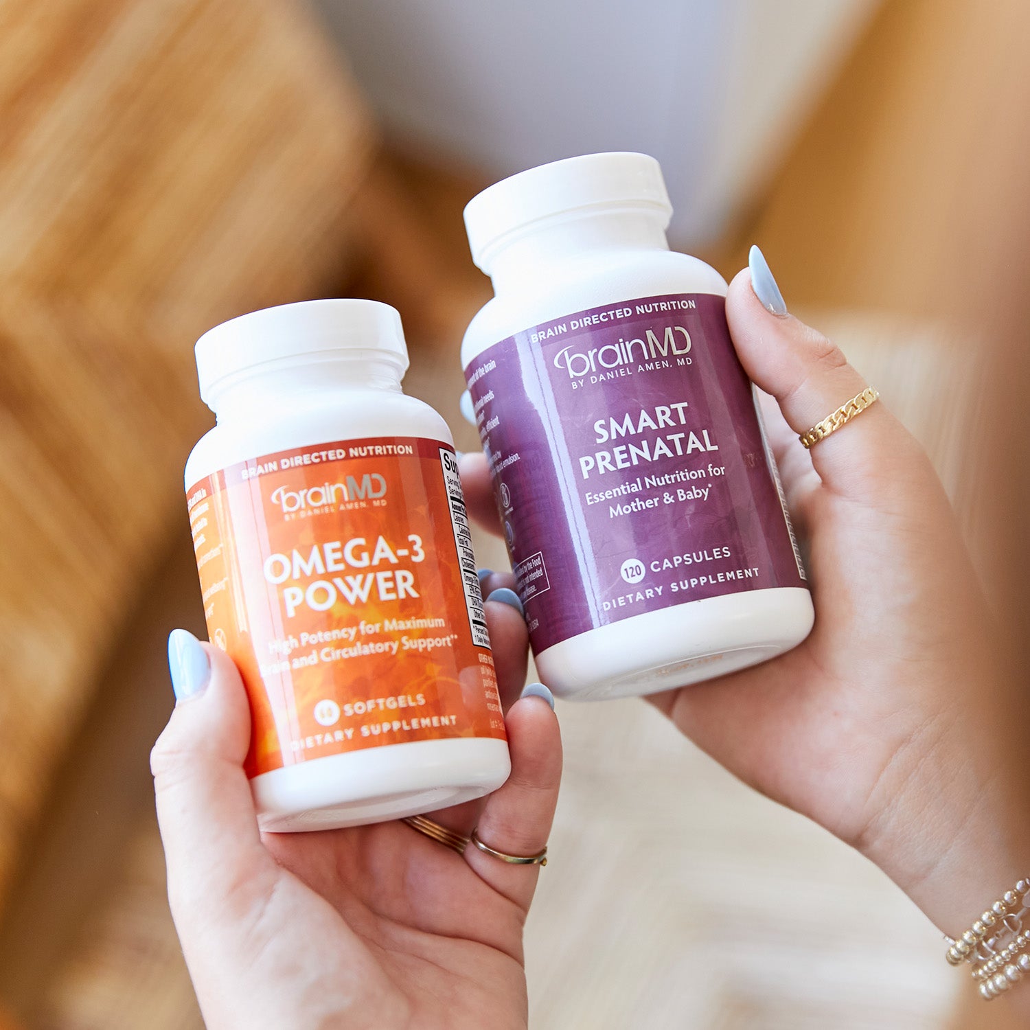 BrainMD Bundle Of Joy: woman holding orange and purple supplement bottles against a blurred interior background