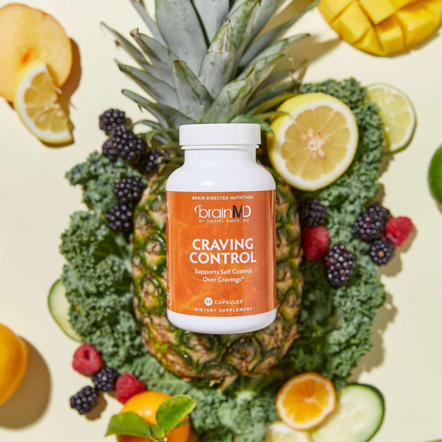 BrainMD Craving Control: orange supplement bottle resting on top of a pineapple with assorted fresh fruits in the background