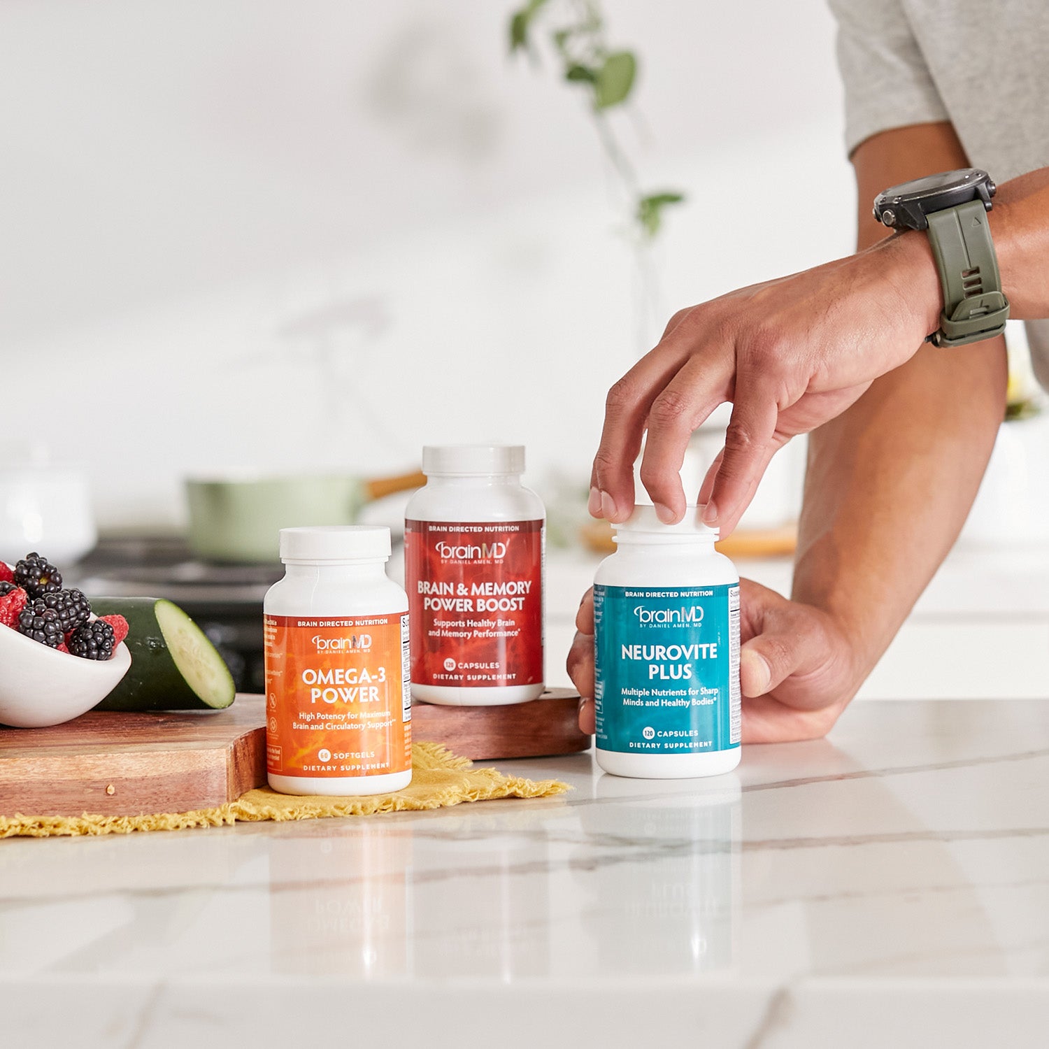 BrainMD Daily Essentials Bundle: 3 supplement bottles of various colors on a kitchen counter, blurred interior background