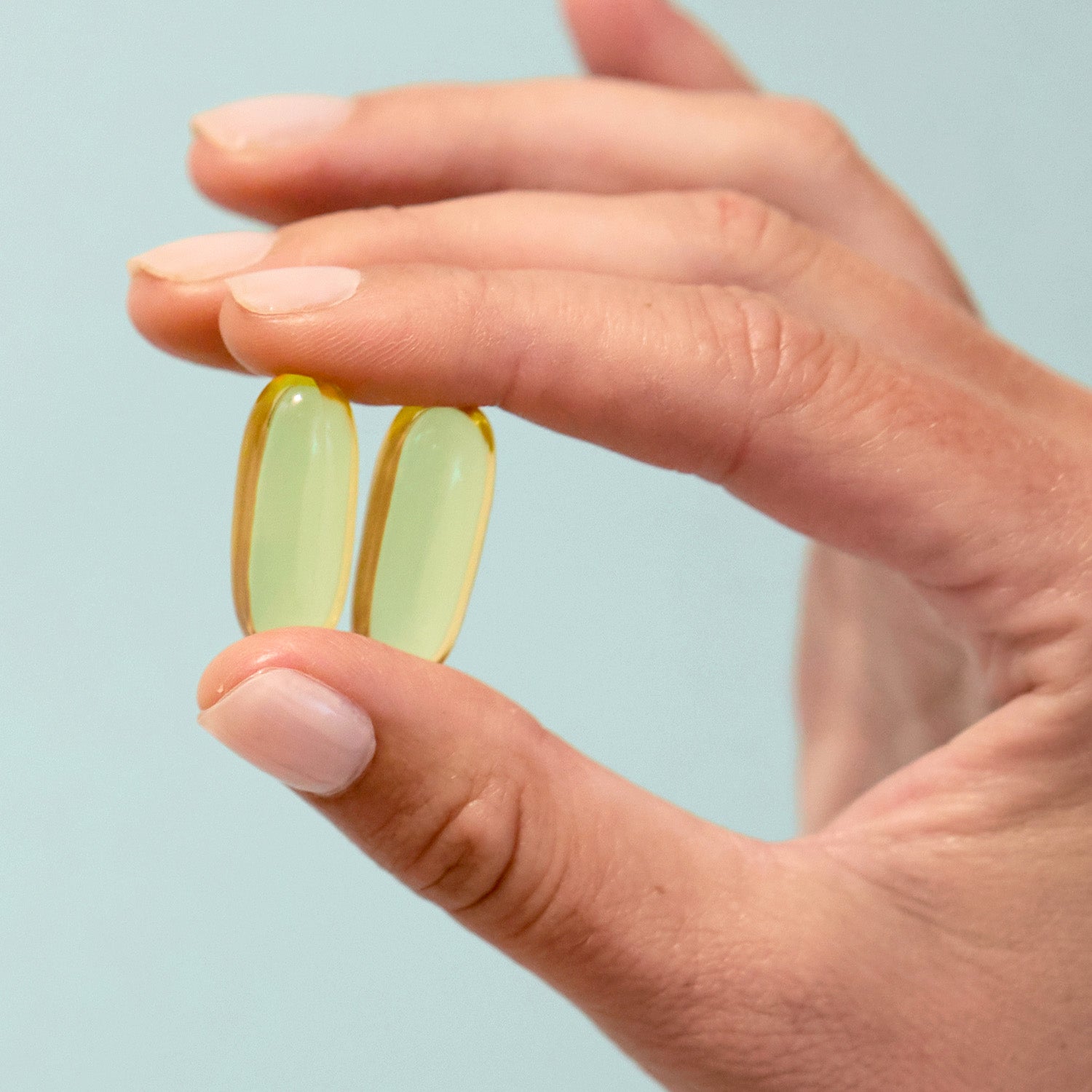 BrainMD Daily Essentials Bundle: person holding 2 golden gelcaps against an off-white background