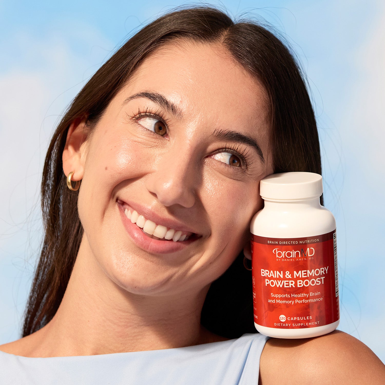 BrainMD Daily Essentials Bundle: woman balances a red supplement bottle on her shoulder, blue sky background