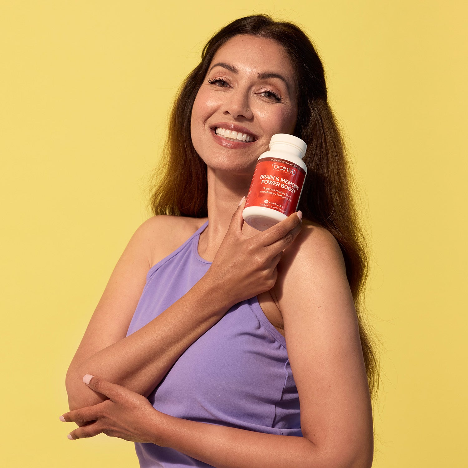 BrainMD Daily Essentials with Squeeze Bundle: smiling woman holds a red supplement bottle against a yellow background