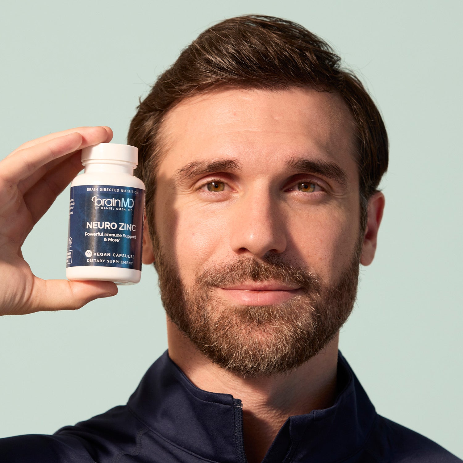 BrainMD Everyday Immunity Bundle: man holding gray bottle next to his face, off-white background