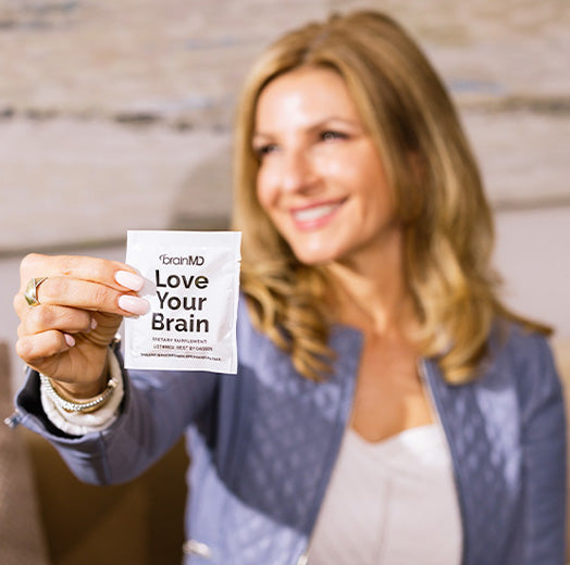 Smiling woman holding a supplement packet that reads "Love Your Brain." Square shape.