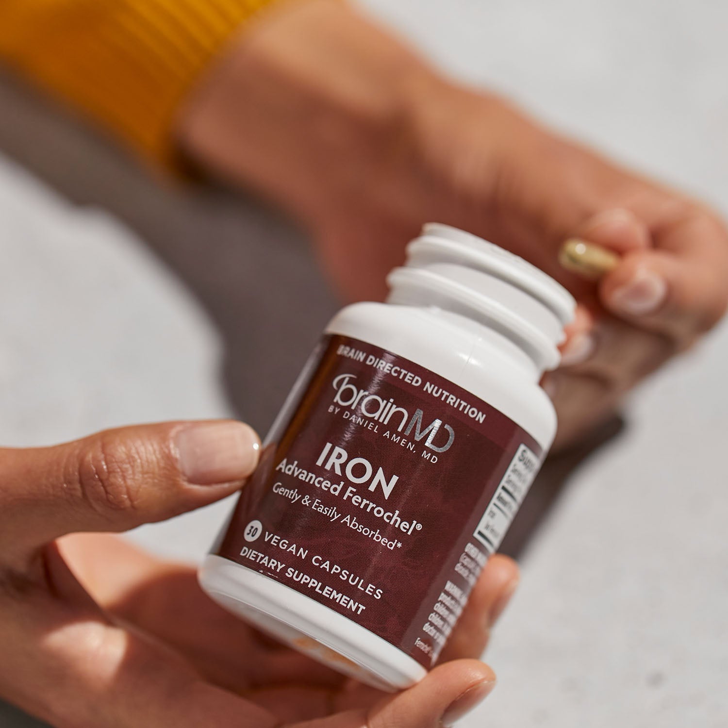 BrainMD Iron: brown supplement bottle in foreground, woman holding capsule against white background
