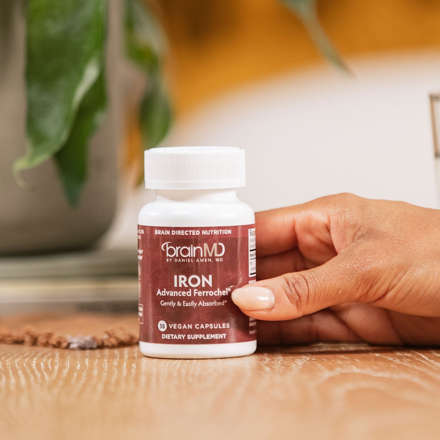 BrainMD Iron: woman's hand holding brown supplement bottle in foreground, blurred interior background