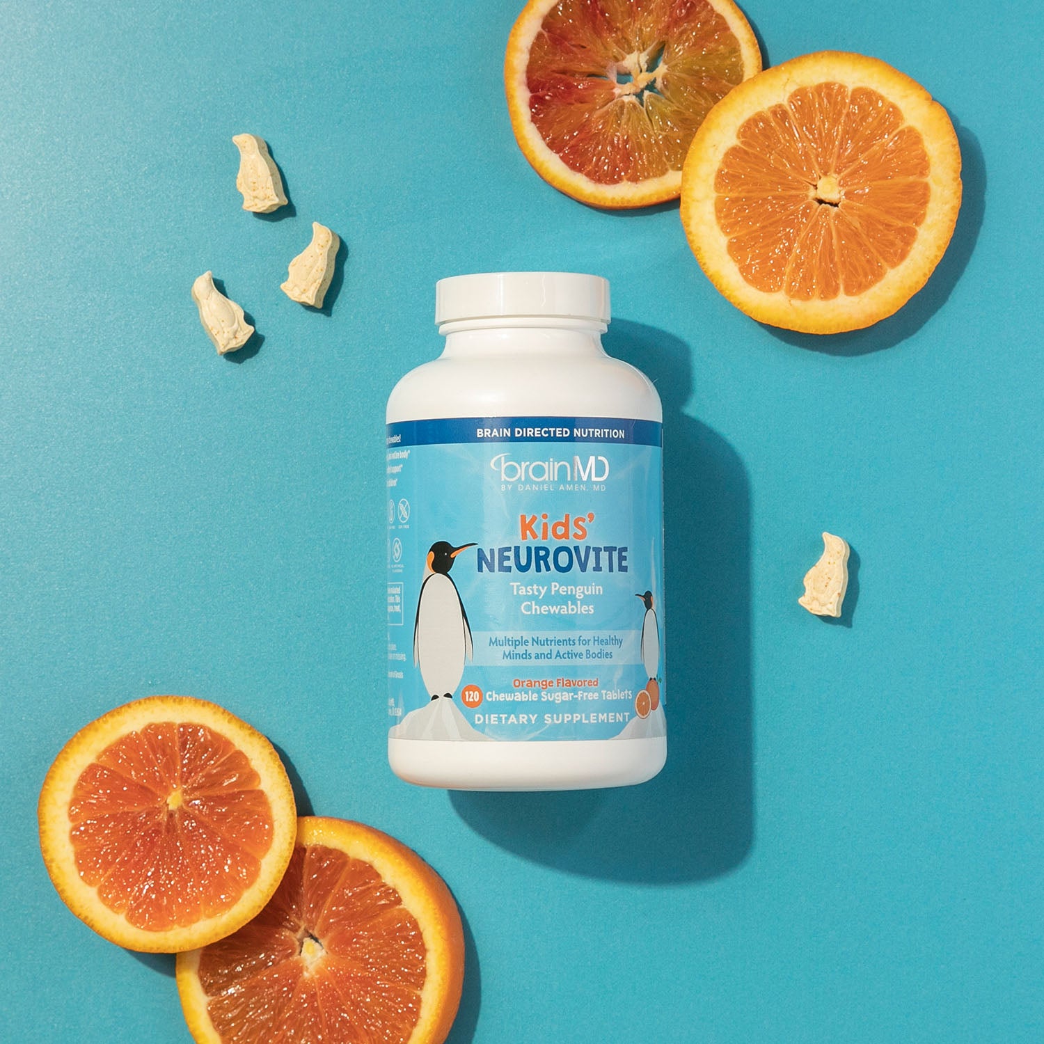 BrainMD Kids' NeuroVite Multivitamin Chewables: bottle, penguin-shaped vitamins and orange slices against a blue background
