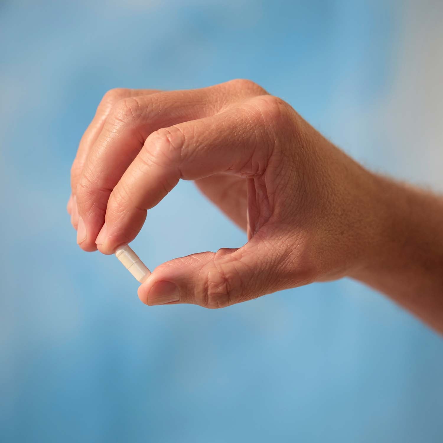 BrainMD Lithium Orotate: person holding a capsule containing white powder in front of a blue-sky background