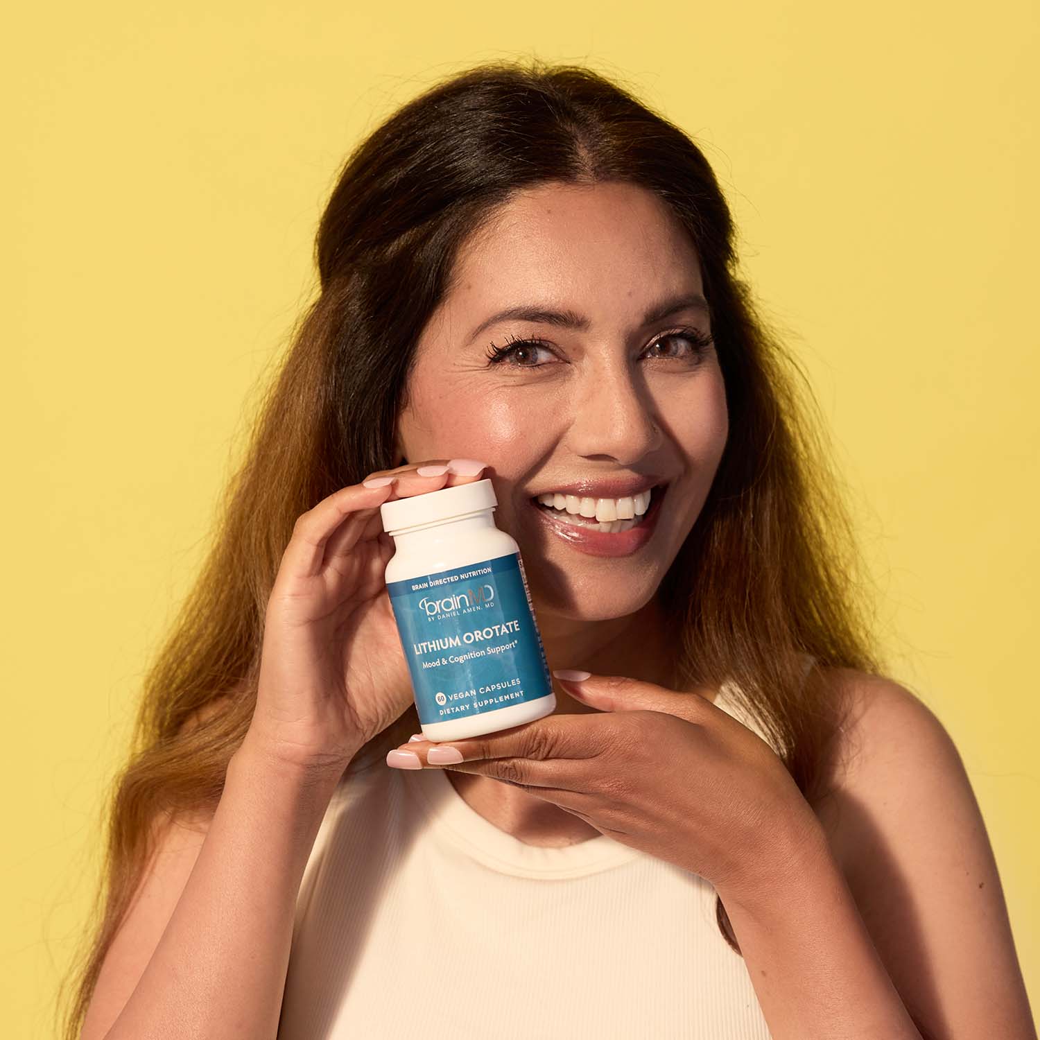 BrainMD Lithium Orotate: smiling woman holding a bottle of Lithium Orotate in front of a yellow background