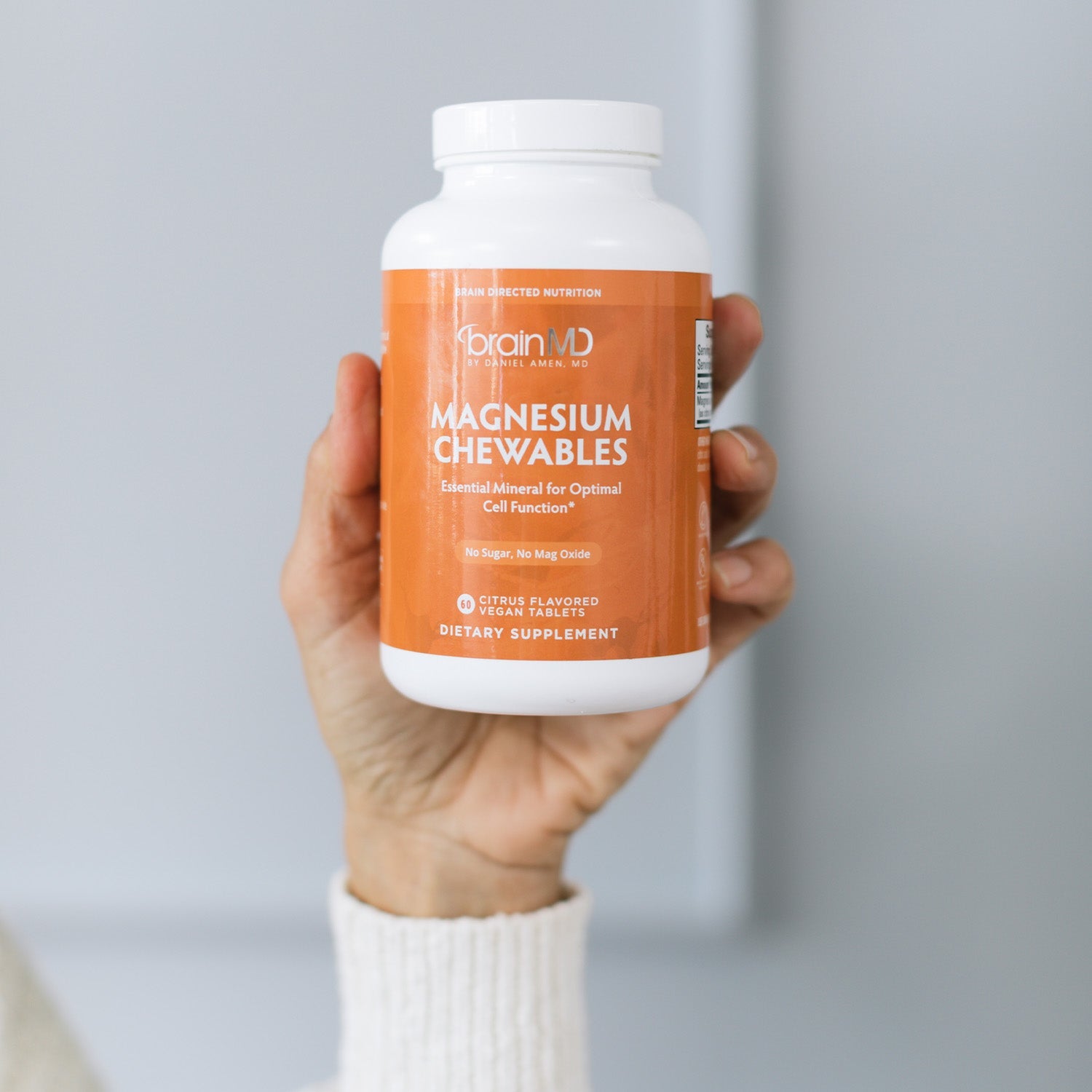 BrainMD Magnesium Chewables: person holding up an orange supplement bottle in front of an off-white background