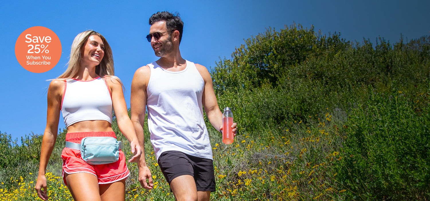 Man and woman walking outdoors with a water bottle, surrounded by greenery.