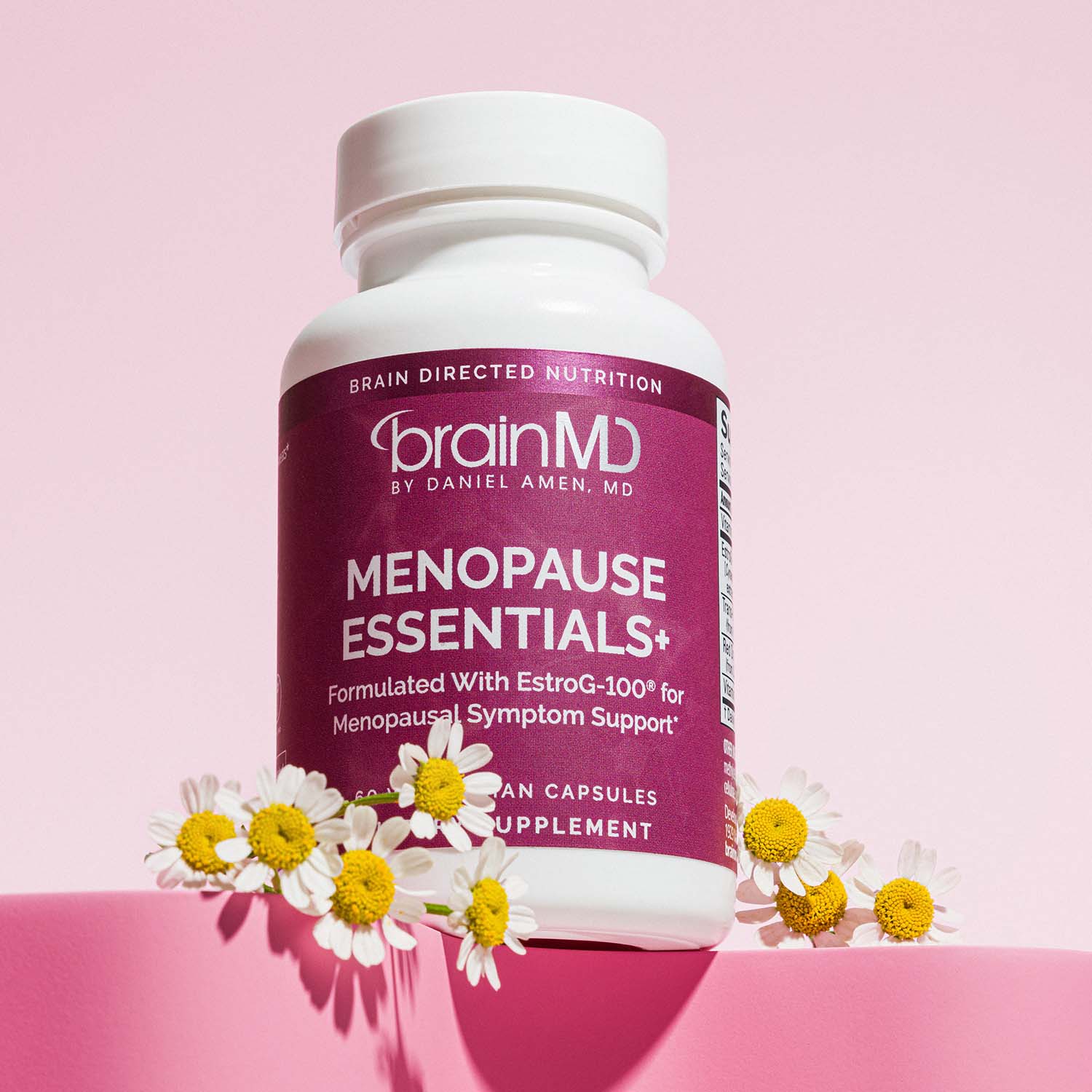 BrainMD Menopause Essentials+: supplement bottle festooned with white flowers at the base set against a light pink background