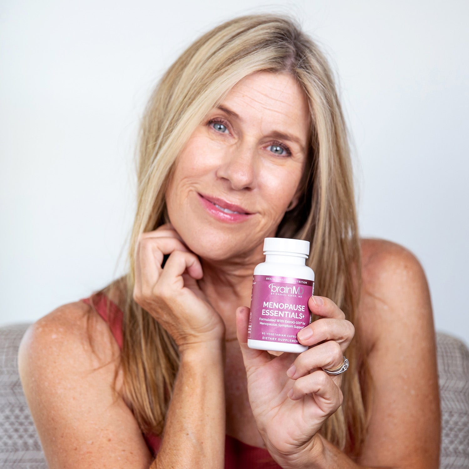 BrainMD Menopause Essentials+: woman holding purple supplement bottle against an off-white background  
