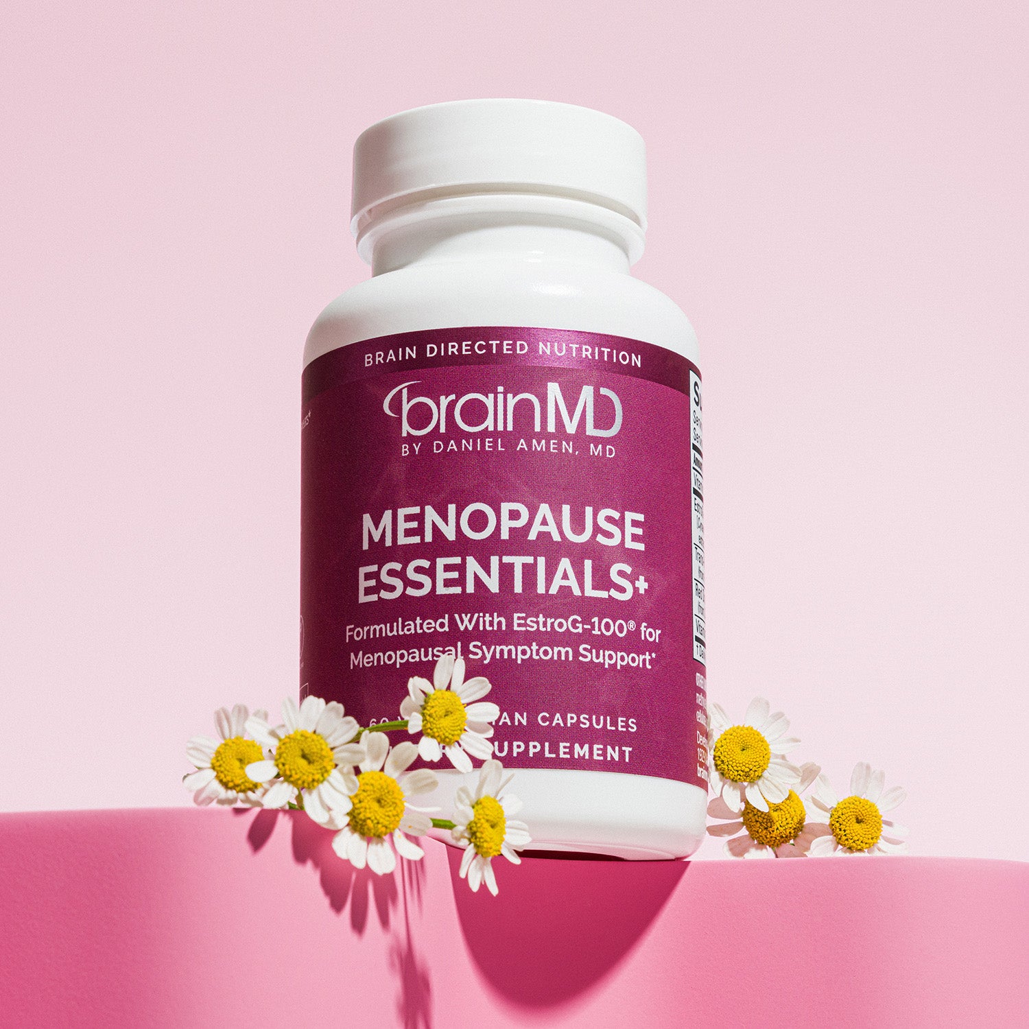 Purple supplement bottle with white flowers at the base against a light pink background.