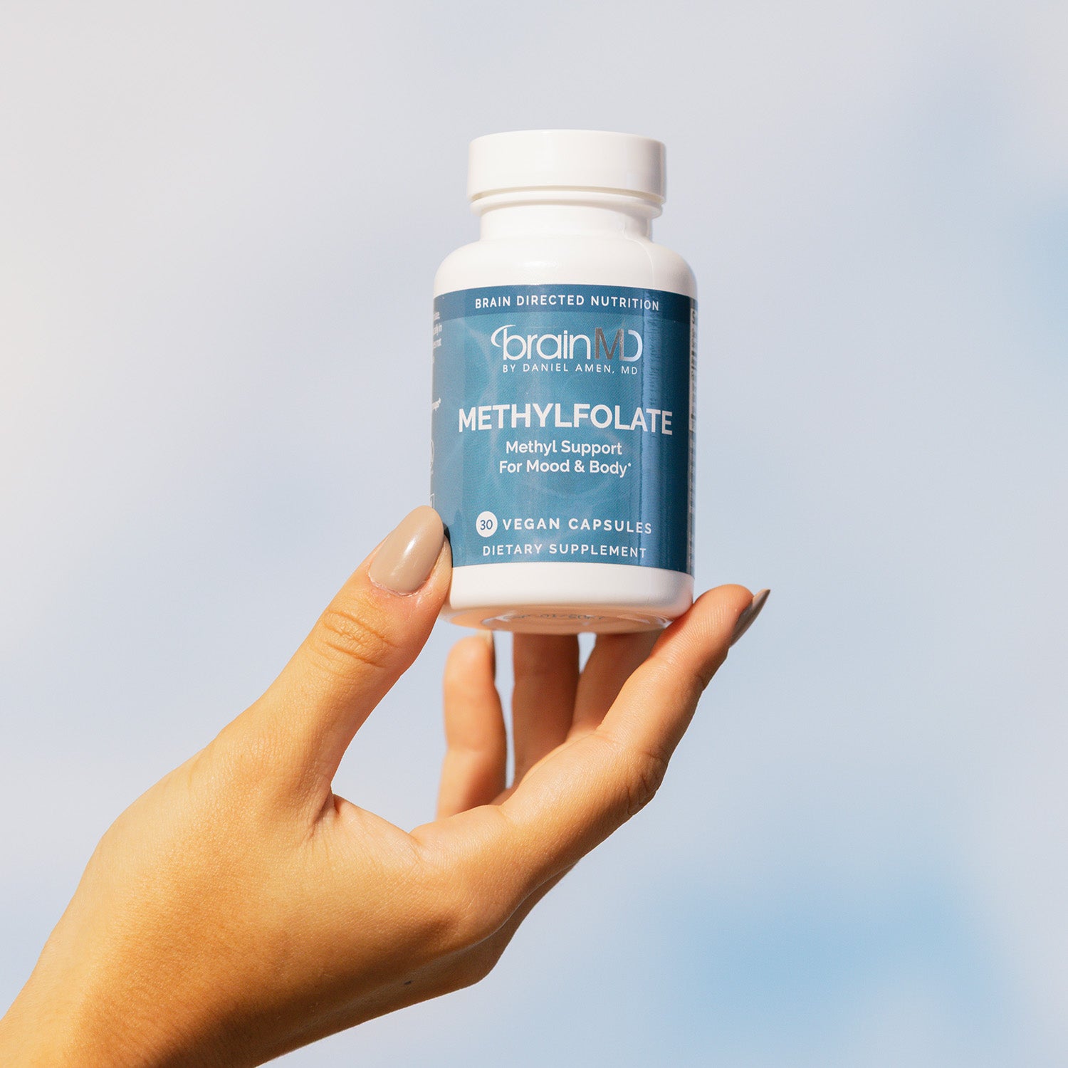 BrainMD Methylfolate: woman's hand holding a supplement bottle against a cloudy sky background