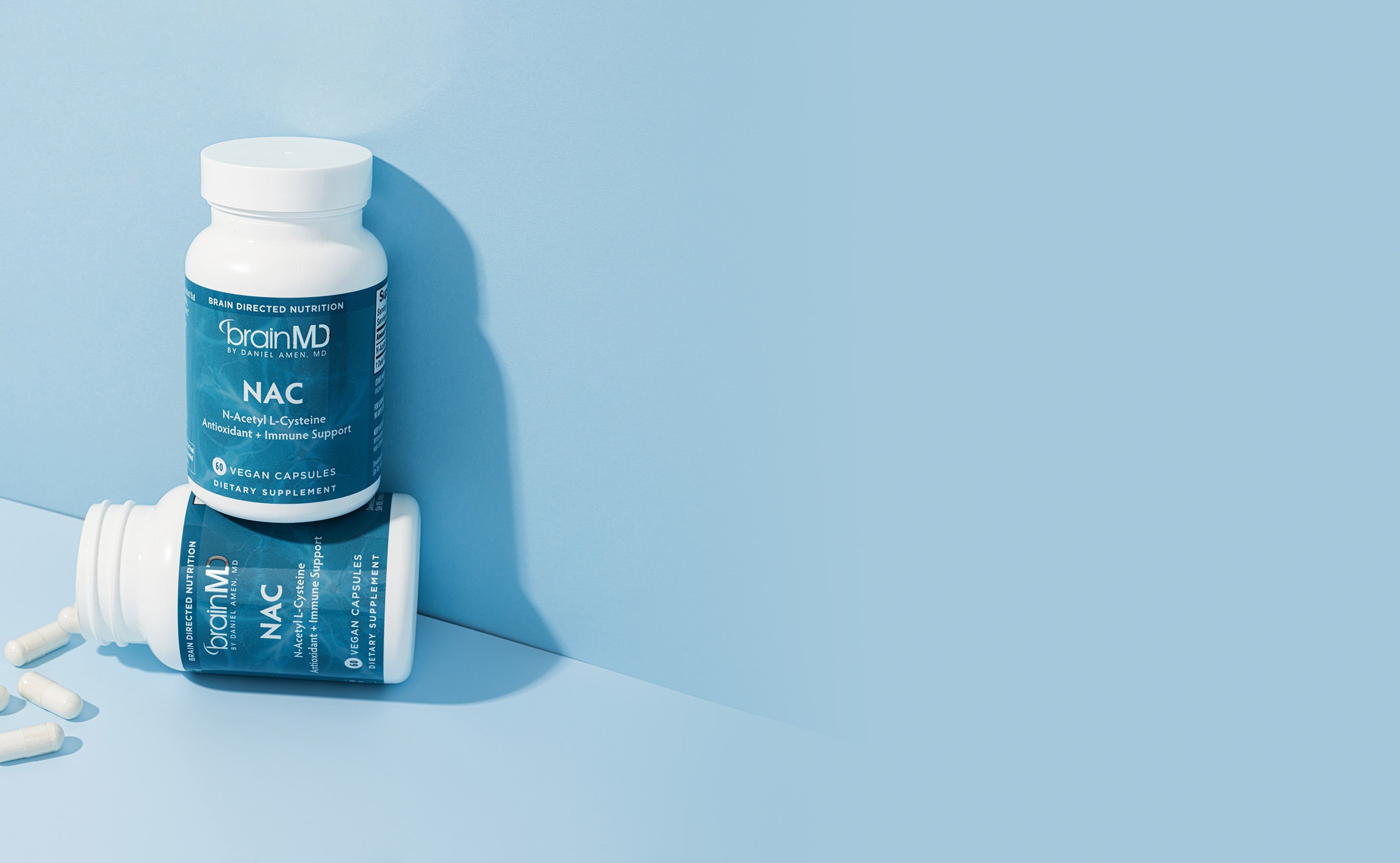 BrainMD NAC (N-Acetyl L-Cysteine): a vertical bottle stands on top of a horizontal bottle against a powder blue background