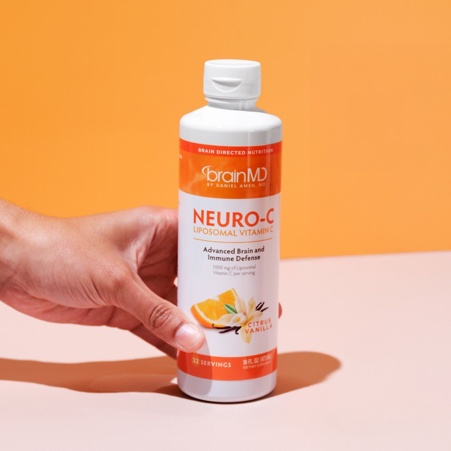 BrainMD Neuro-C Vitamin C: hand grabbing bottle of liposomal vitamin C in front of an orange background