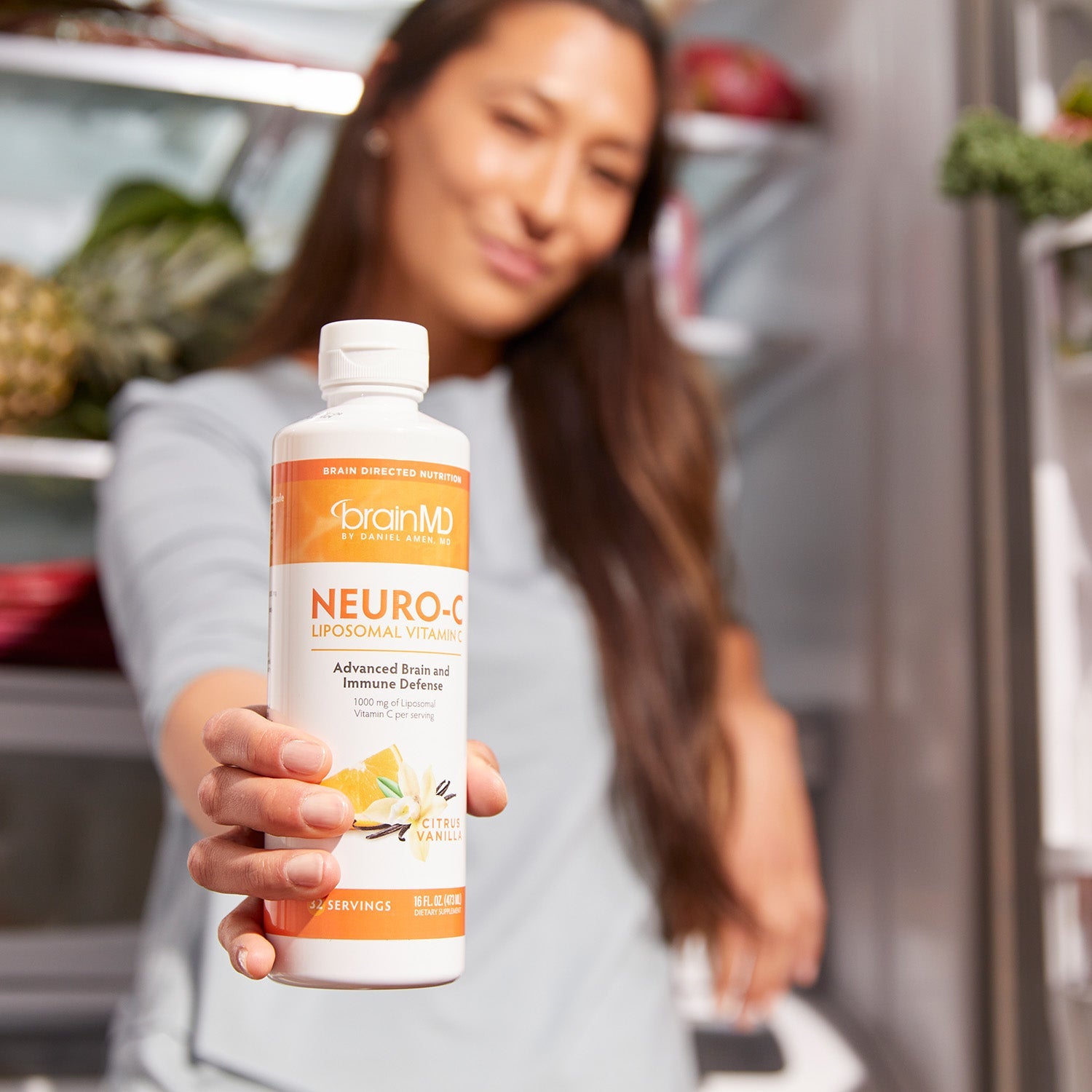 BrainMD Neuro-C Vitamin C: blurred woman in background holding an orange and white supplement bottle toward the camera