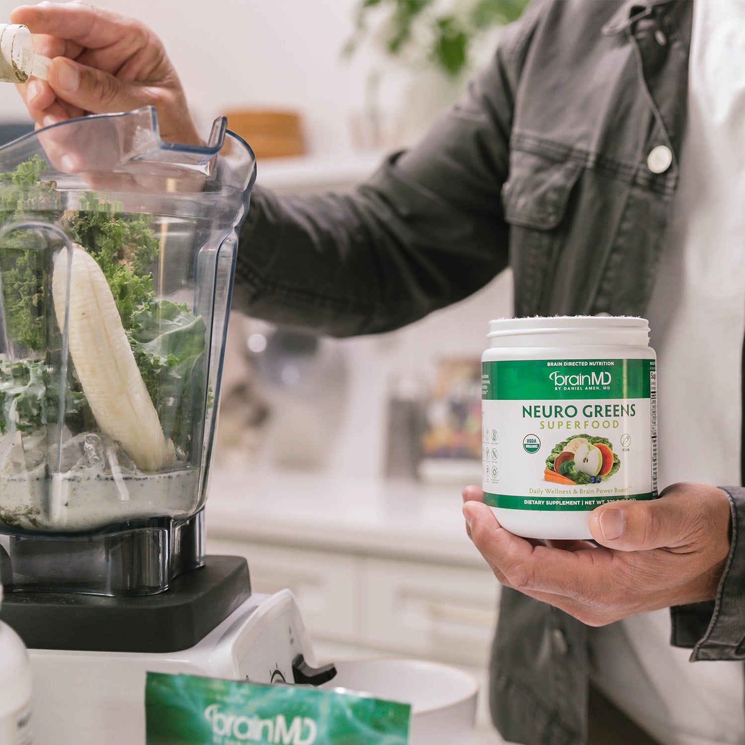 BrainMD Neuro Greens Superfood powder: man holding a container, dropping a scoop of powder into a blender