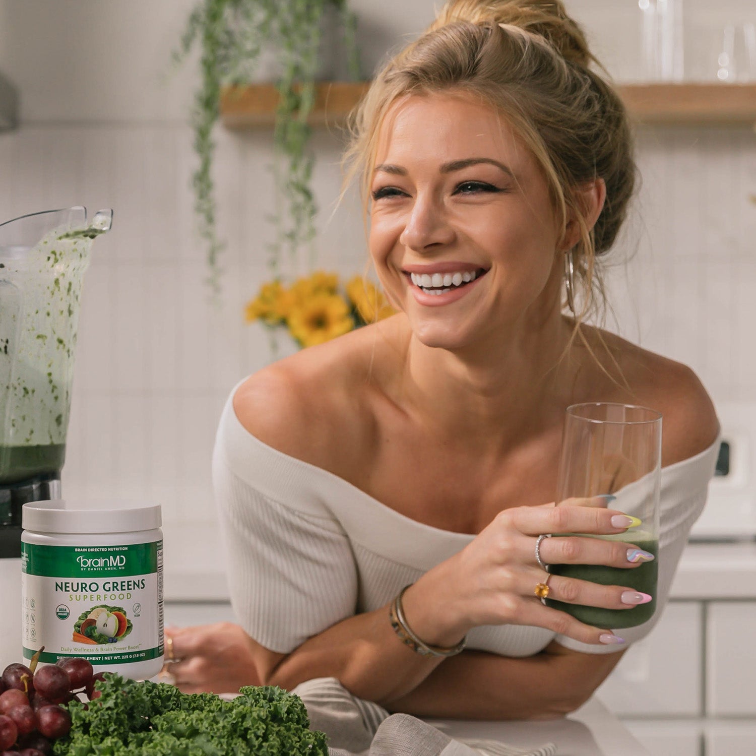 BrainMD Neuro Greens Superfood: smiling woman with a glass of green juice in a kitchen
