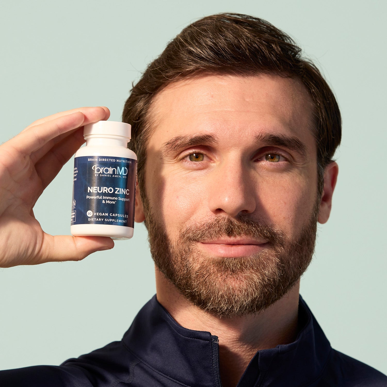 BrainMD Neuro Zinc: man holding gray supplement bottle next to his face in front of an off-white background