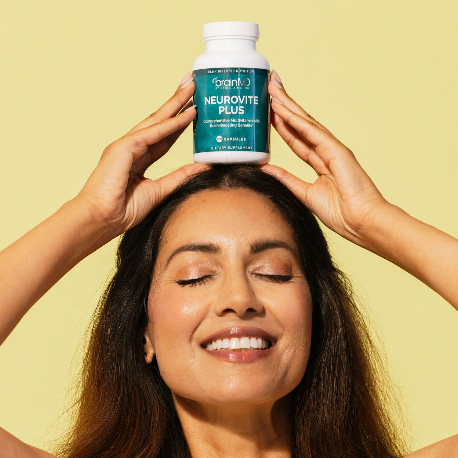 BrainMD NeuroVite Plus Multivitamin: woman balancing a supplement bottle on her head in front of a yellow background