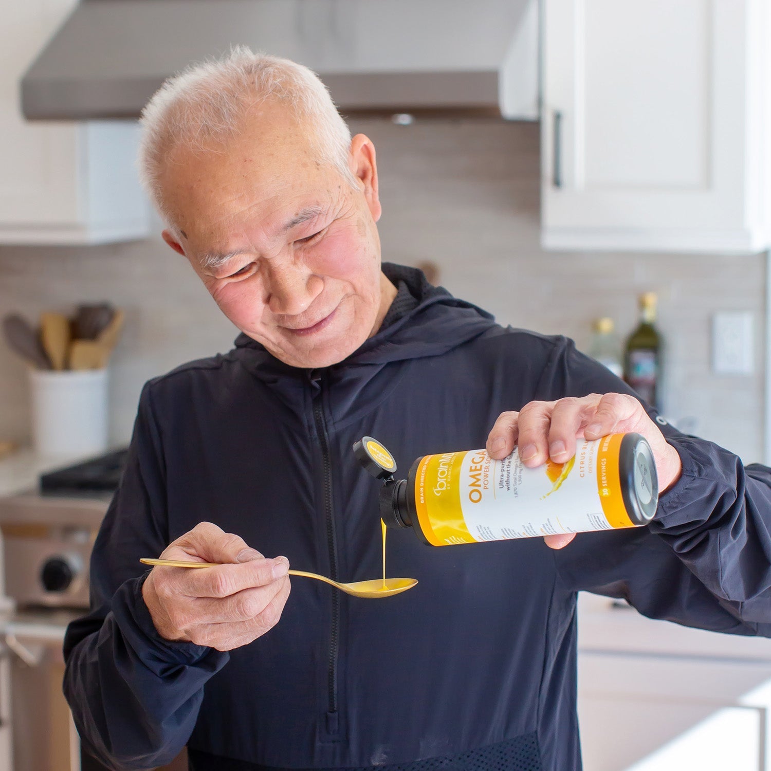 BrainMD Omega-3 Power Squeeze: man pouring liquid from an orange and white bottle into a spoon, blurred kitchen background