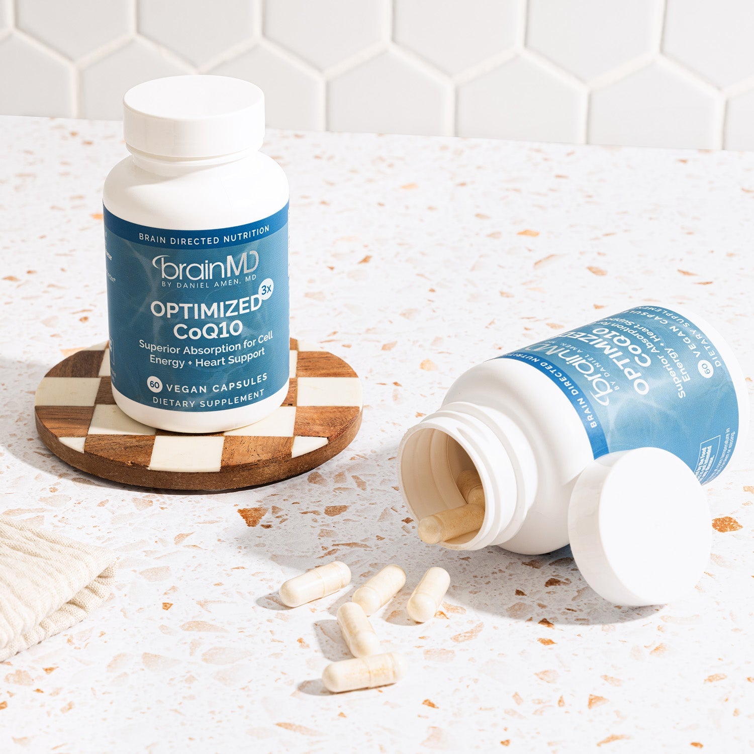 BrainMD Optimized CoQ10: two blue supplement bottles, one rests on its side spilling capsules onto a white counter
