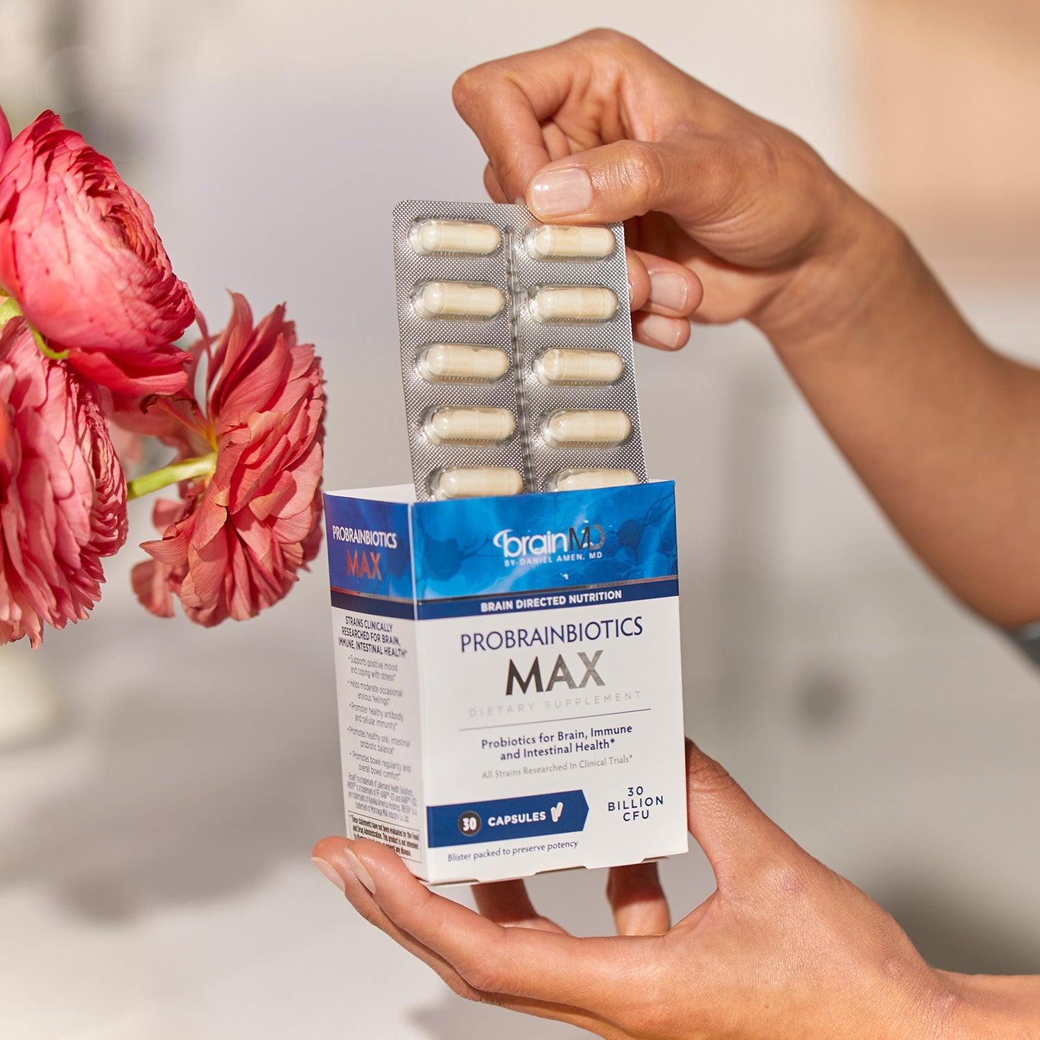 BrainMD ProBrainBiotics MAX: person pulling packaged capsules out of a blue & white supplement box with a blurred background
