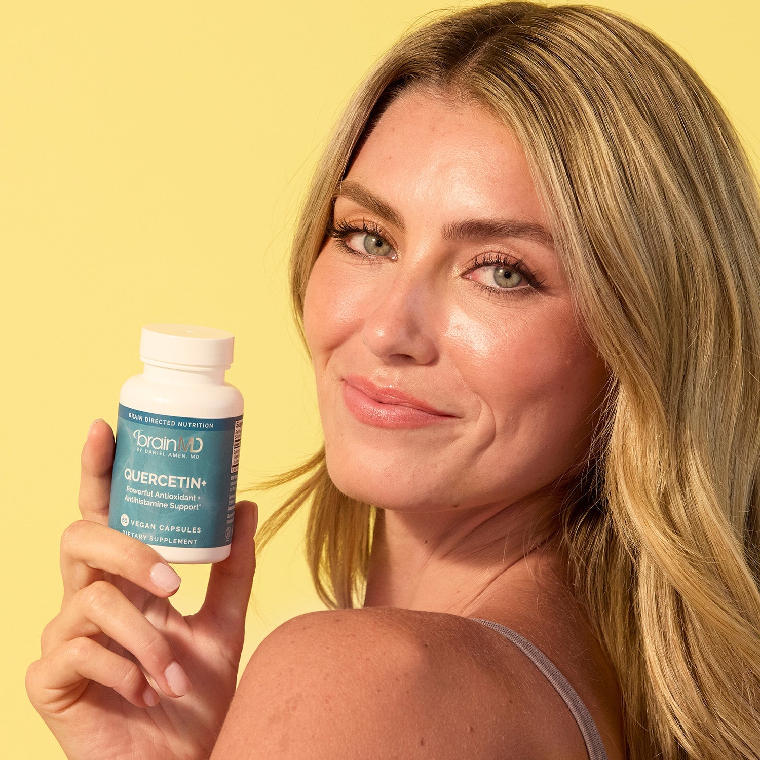 BrainMD Quercetin+: woman holding blue supplement bottle against a yellow background