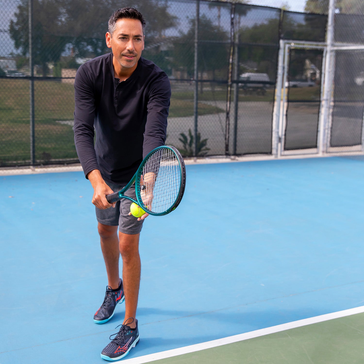 Lifestyle image: man on a tennis court preparing to serve.