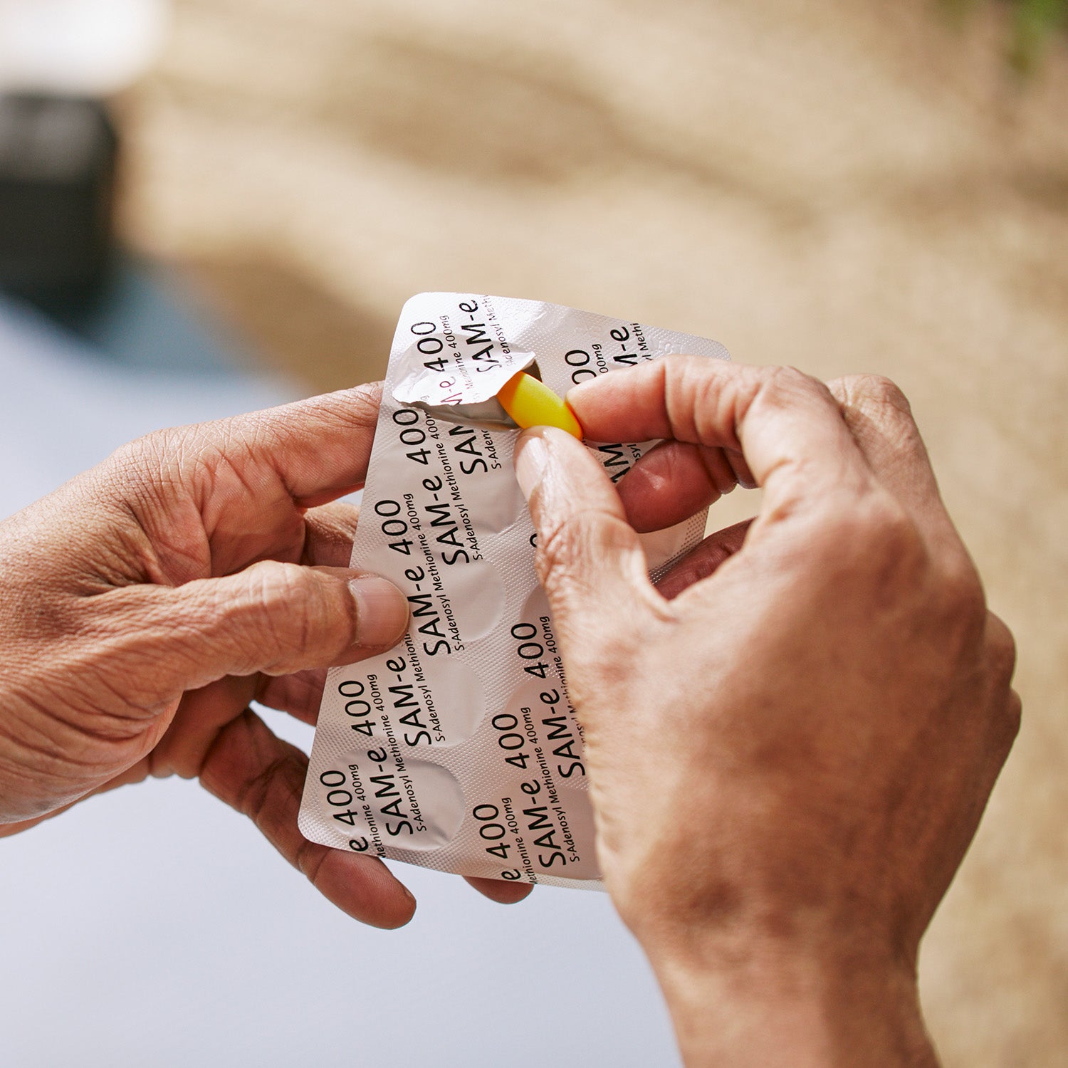 Person taking a yellow supplement tablet out of a foil blister.