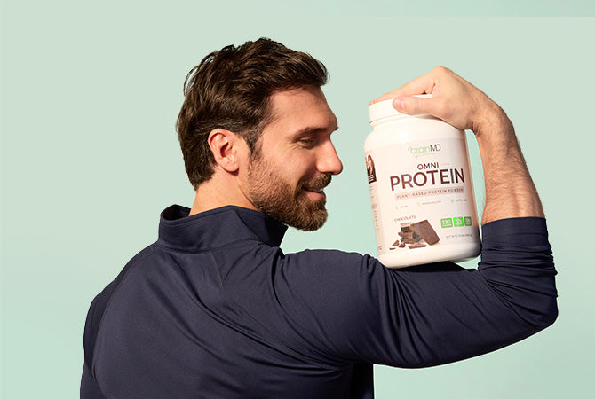Smiling man holding a container of OMNI Protein powder against his flexed bicep.
